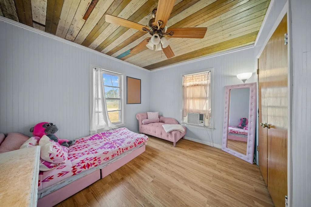 The room features hardwood style flooring, light blue paneled walls, and a multi-toned wood plank ceiling with a ceiling fan