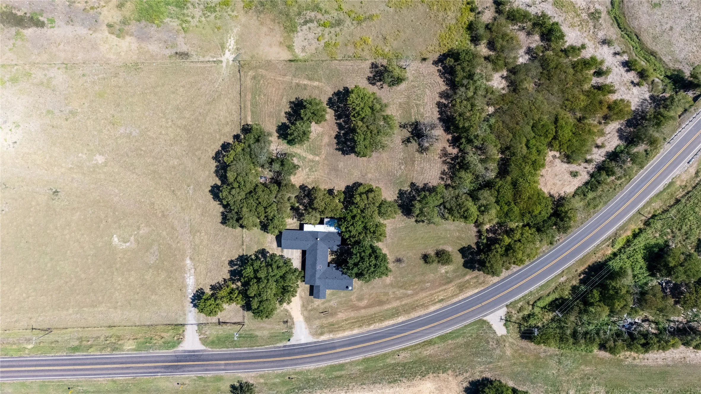 The property includes a residence with a dark roof, surrounded by mature trees, and is situated near a paved road