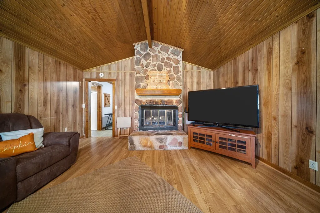 Living area featuring wood paneling on the walls and vaulted ceiling, a stone fireplace, and wood flooring