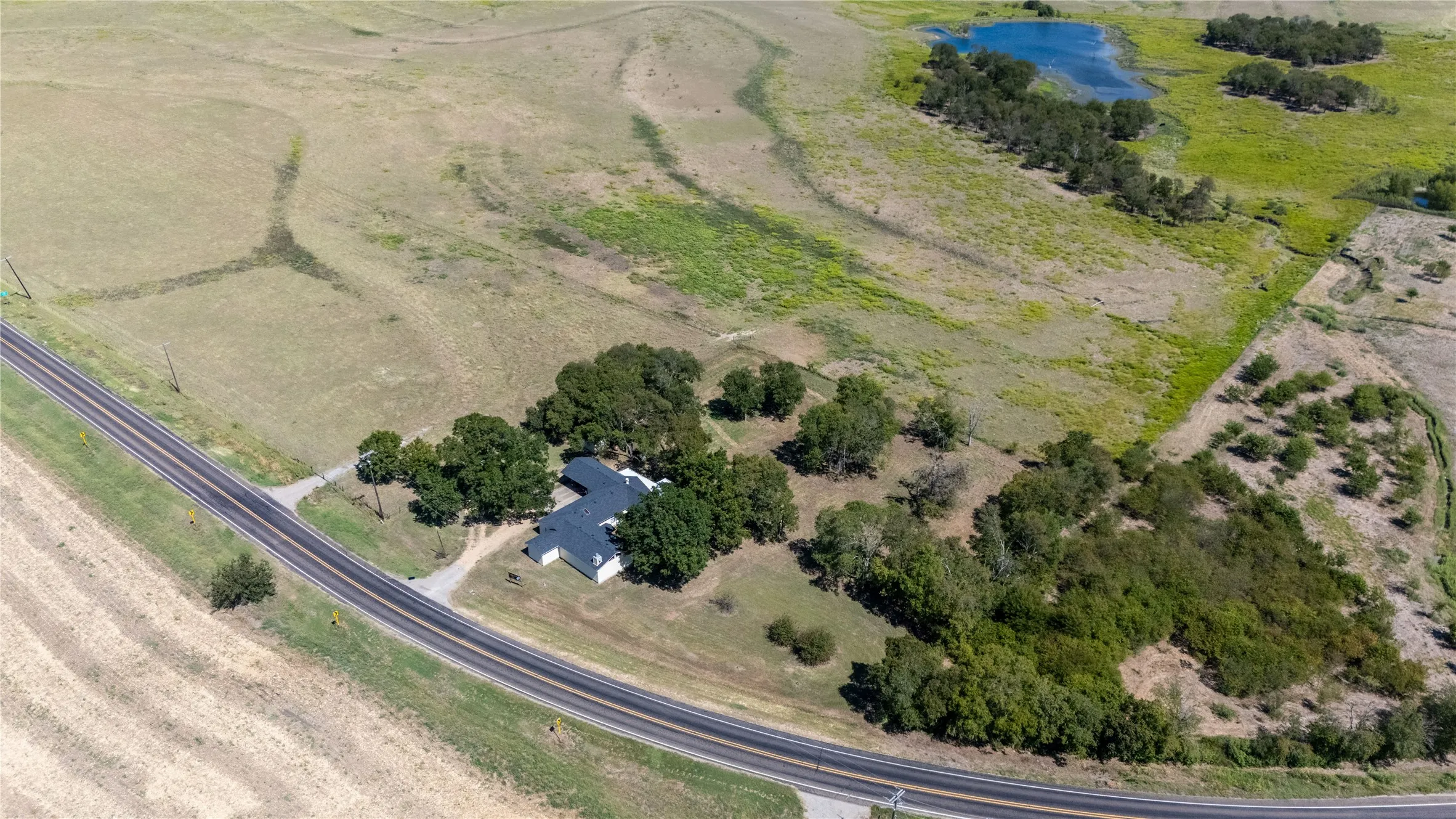 Aerial view showcasing the property situated amidst expansive open land, featuring a visible pond and surrounding trees