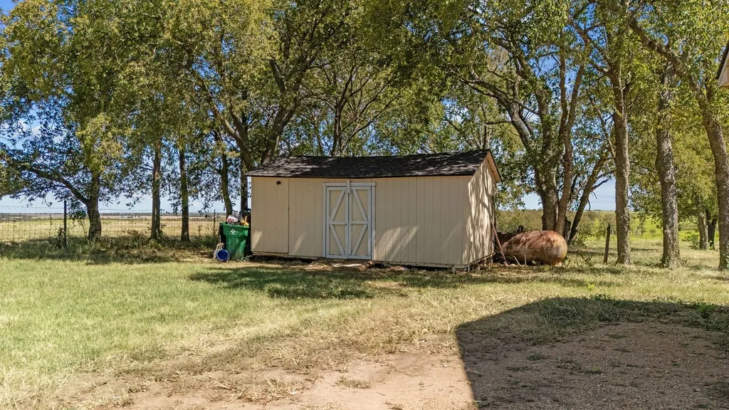 The property features a useful outdoor storage shed with double doors, situated within a yard that includes mature trees and a grassy area