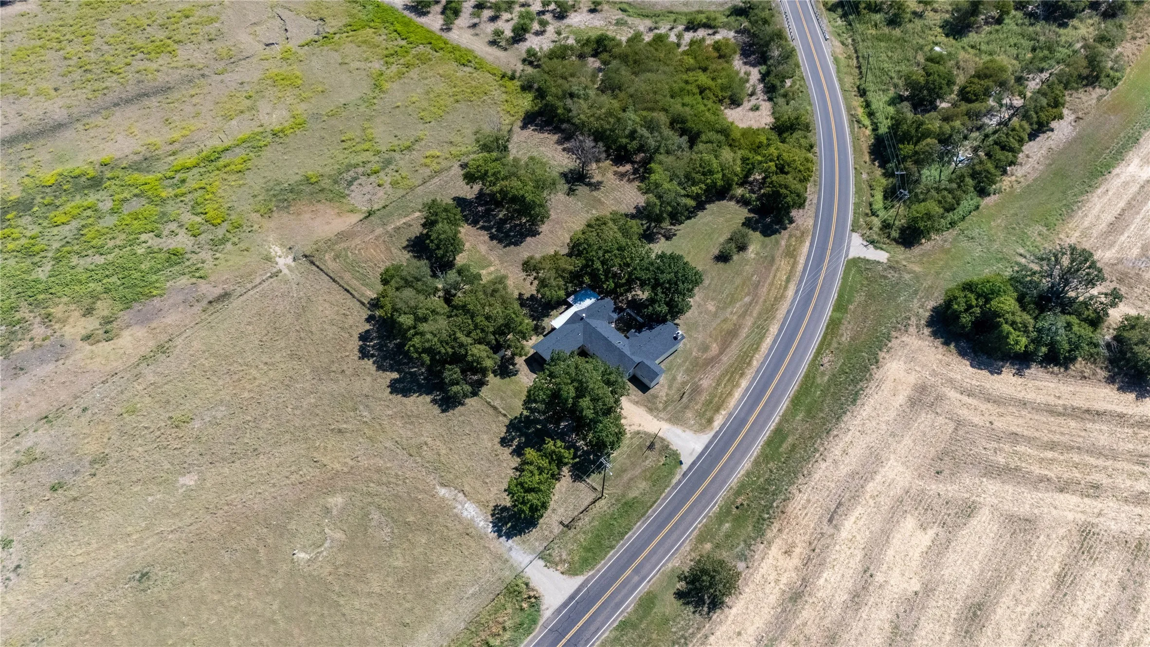 The property features a residence surrounded by mature trees, situated alongside a paved road, with expansive land on both sides