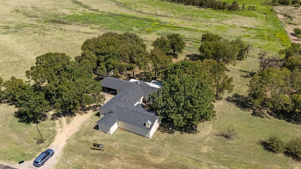 The property features a single-story dwelling with a dark shingled roof, surrounded by extensive green grounds with numerous mature trees