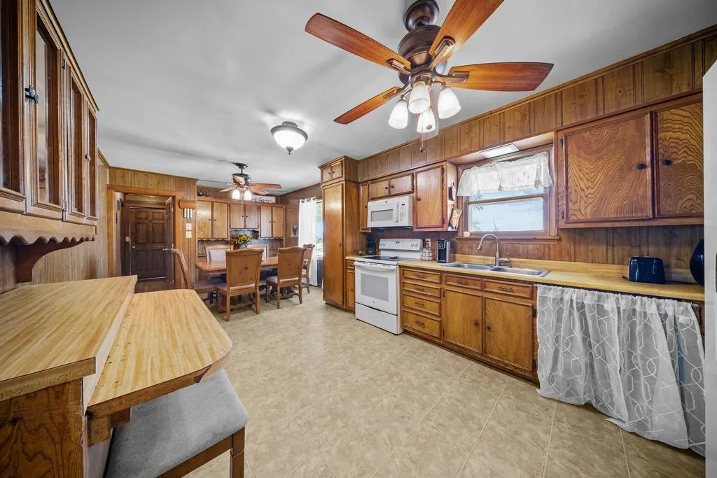 The kitchen features wood cabinetry, a ceiling fan with integrated lighting, and a white oven and microwave