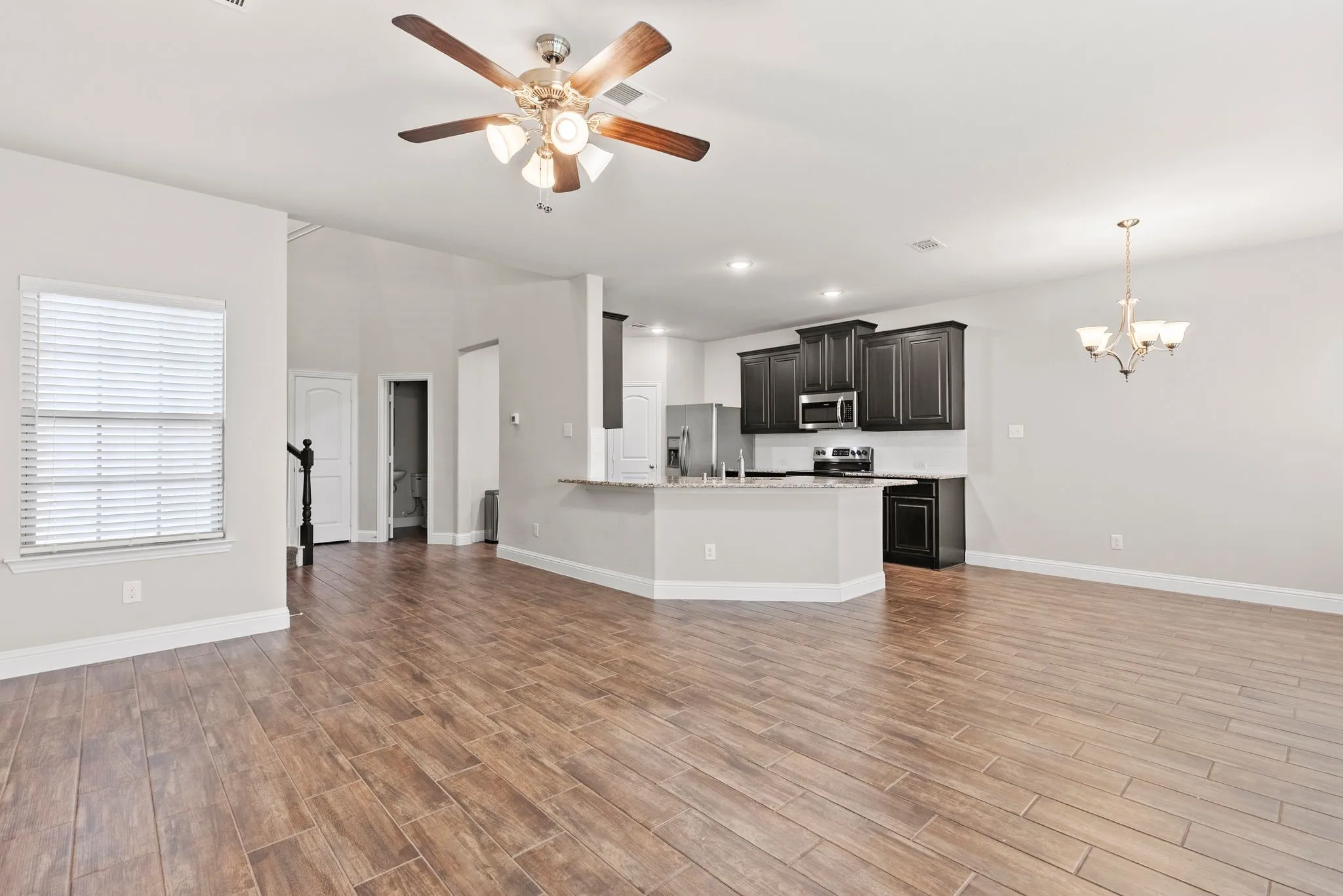 This open-concept living area features wood-look tile flooring, light grey walls, and a ceiling fan with integrated lighting