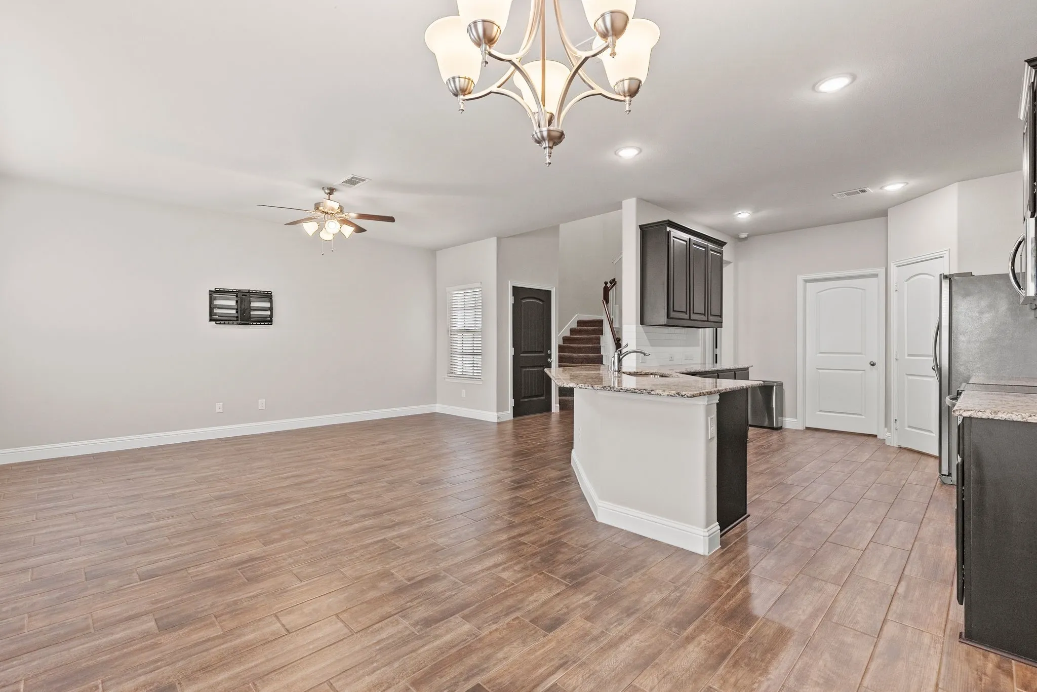 Spacious open-concept living area featuring wood-look tile flooring, a ceiling fan, and a chandelier