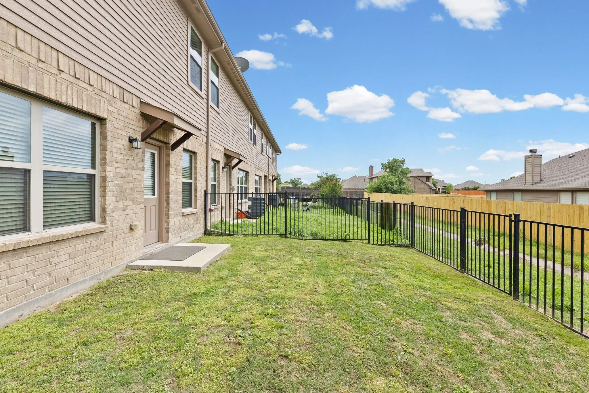 The property features a private yard with a lawn and black metal fencing, extending along the side and rear