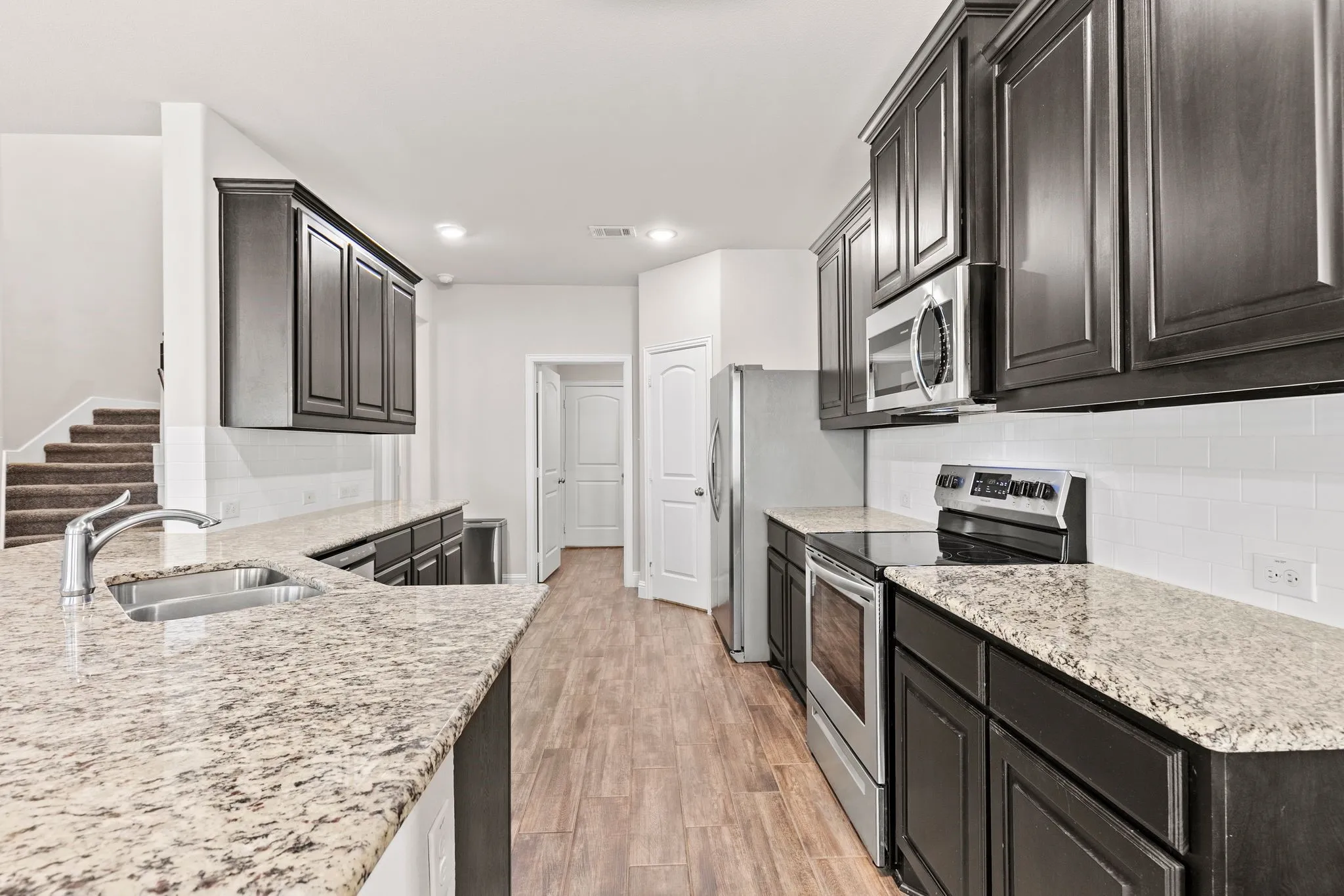 The kitchen features granite countertops, dark wood cabinetry, a stainless steel sink with a gooseneck faucet, a white subway tile backsplash, and stainless steel appliances including an oven, microwave, and dishwasher