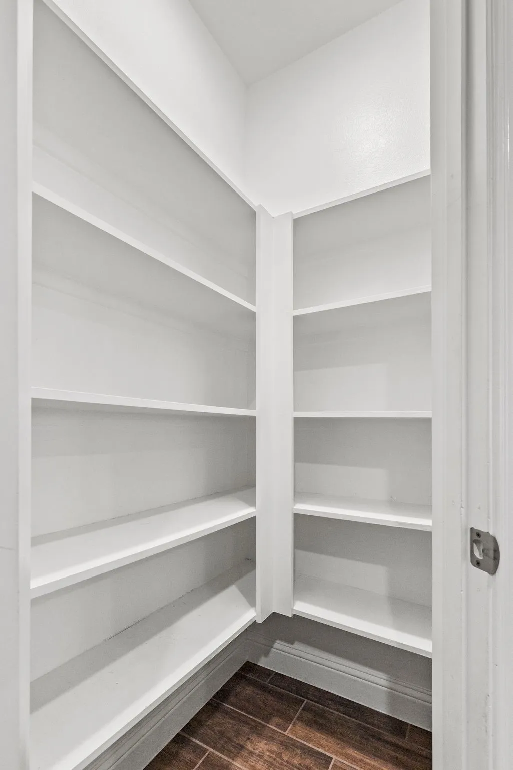 This well-appointed walk-in pantry features extensive white shelving, providing ample storage, and is complemented by dark wood-look flooring