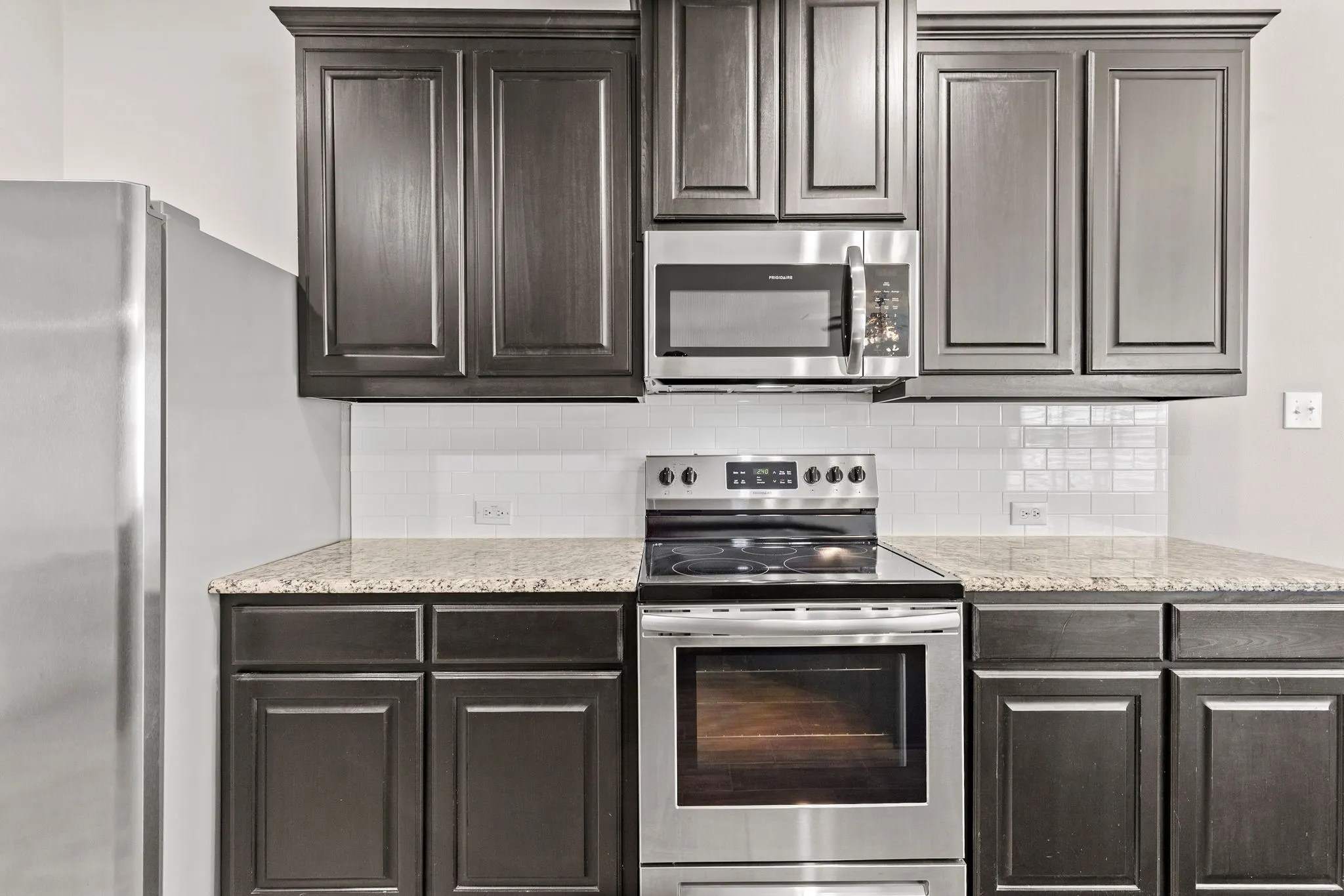 The kitchen features dark wood cabinetry, stainless steel appliances, granite countertops, and a white subway tile backsplash