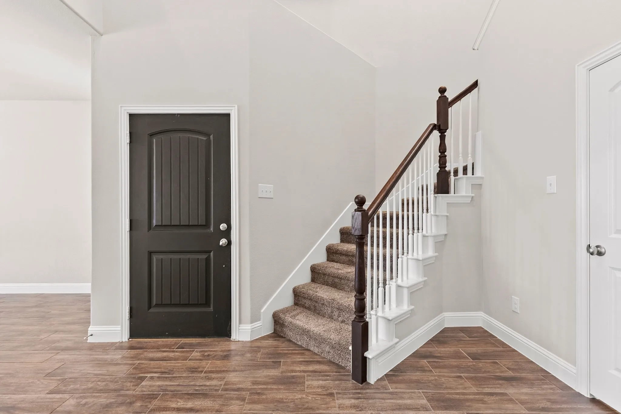 Entryway featuring wood-look tile flooring, a dark paneled door, and a staircase with a carpeted runner and white balusters