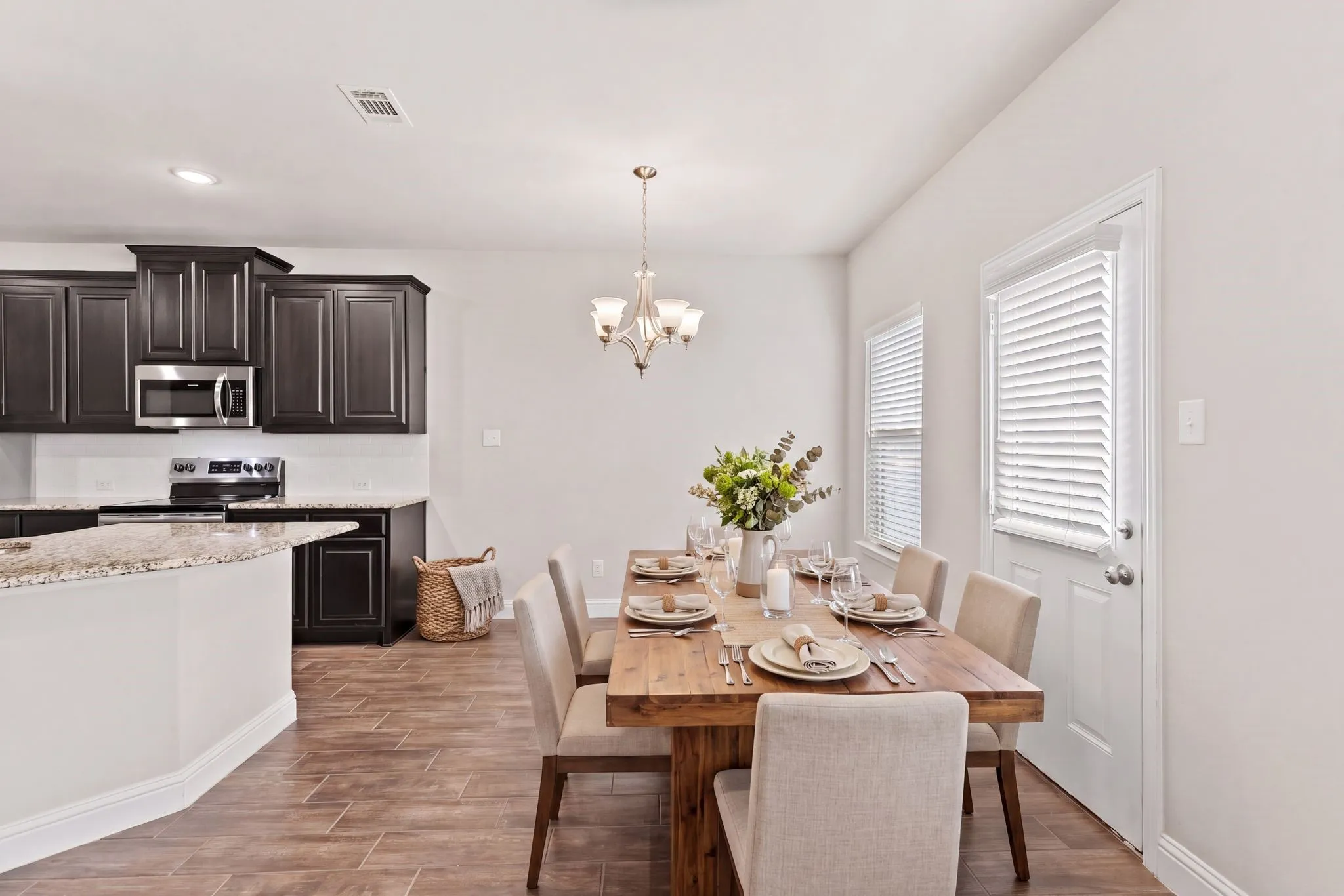 The open-concept design integrates a dining area with a modern kitchen, featuring dark wood cabinetry, stainless steel appliances, and granite countertops