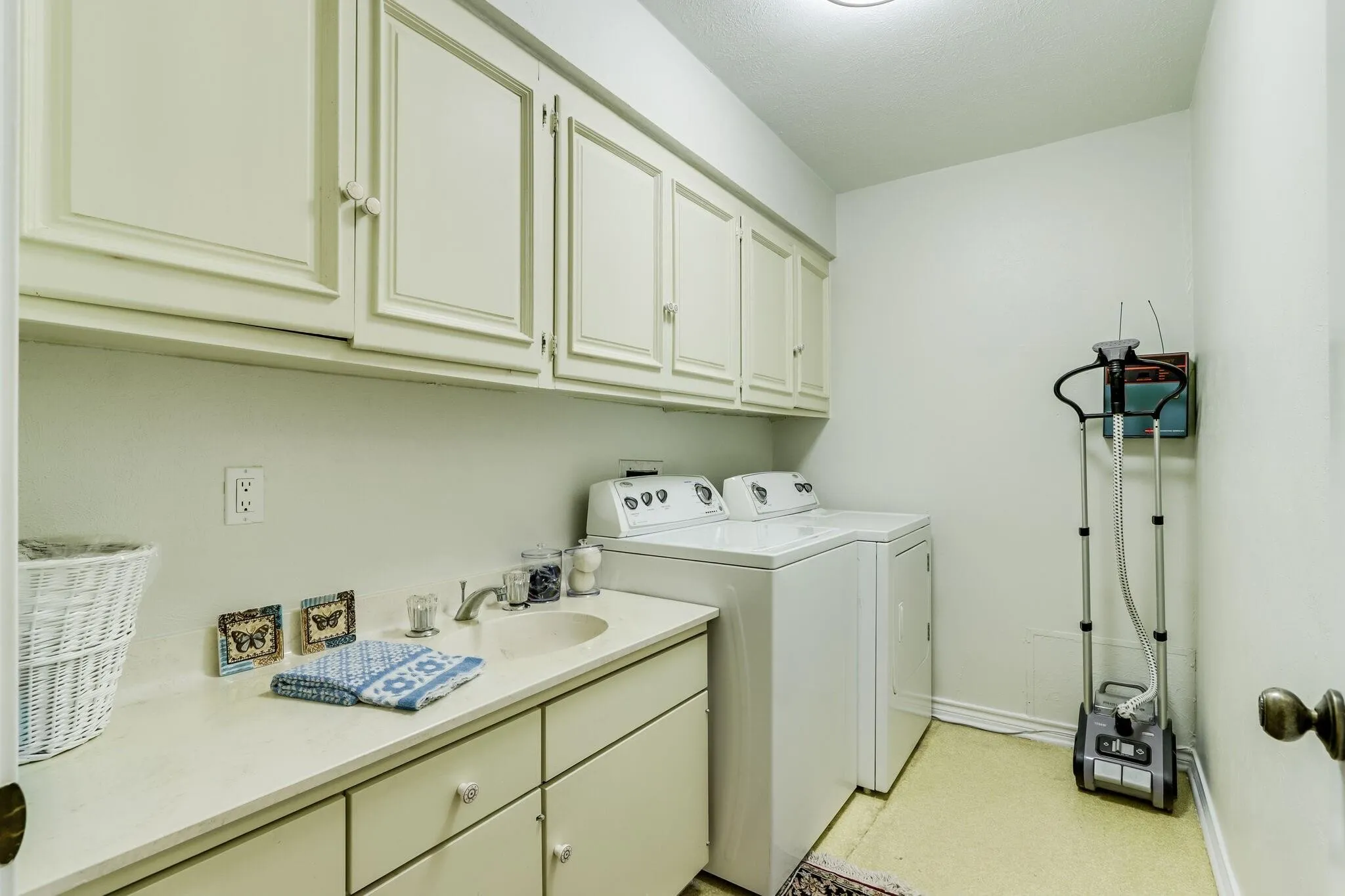 Utility room with upper and lower cabinetry, an integrated countertop sink, and space for laundry appliances