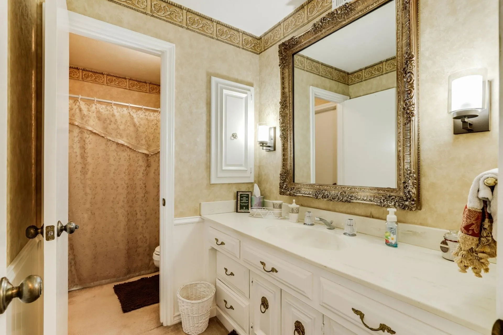 Bathroom featuring a single vanity with a white countertop, classic white cabinetry, ornate wall mirror, and dual wall sconces
