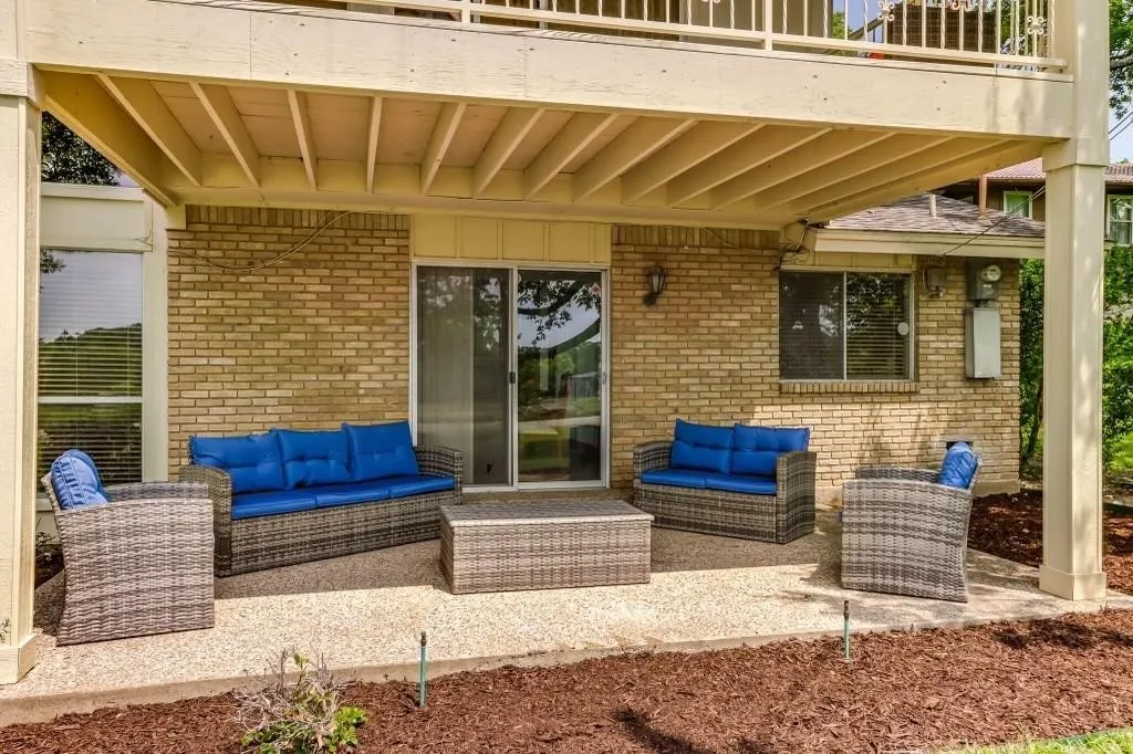 Covered patio with a textured concrete surface under a second-story deck, featuring a brick exterior wall and sliding glass door