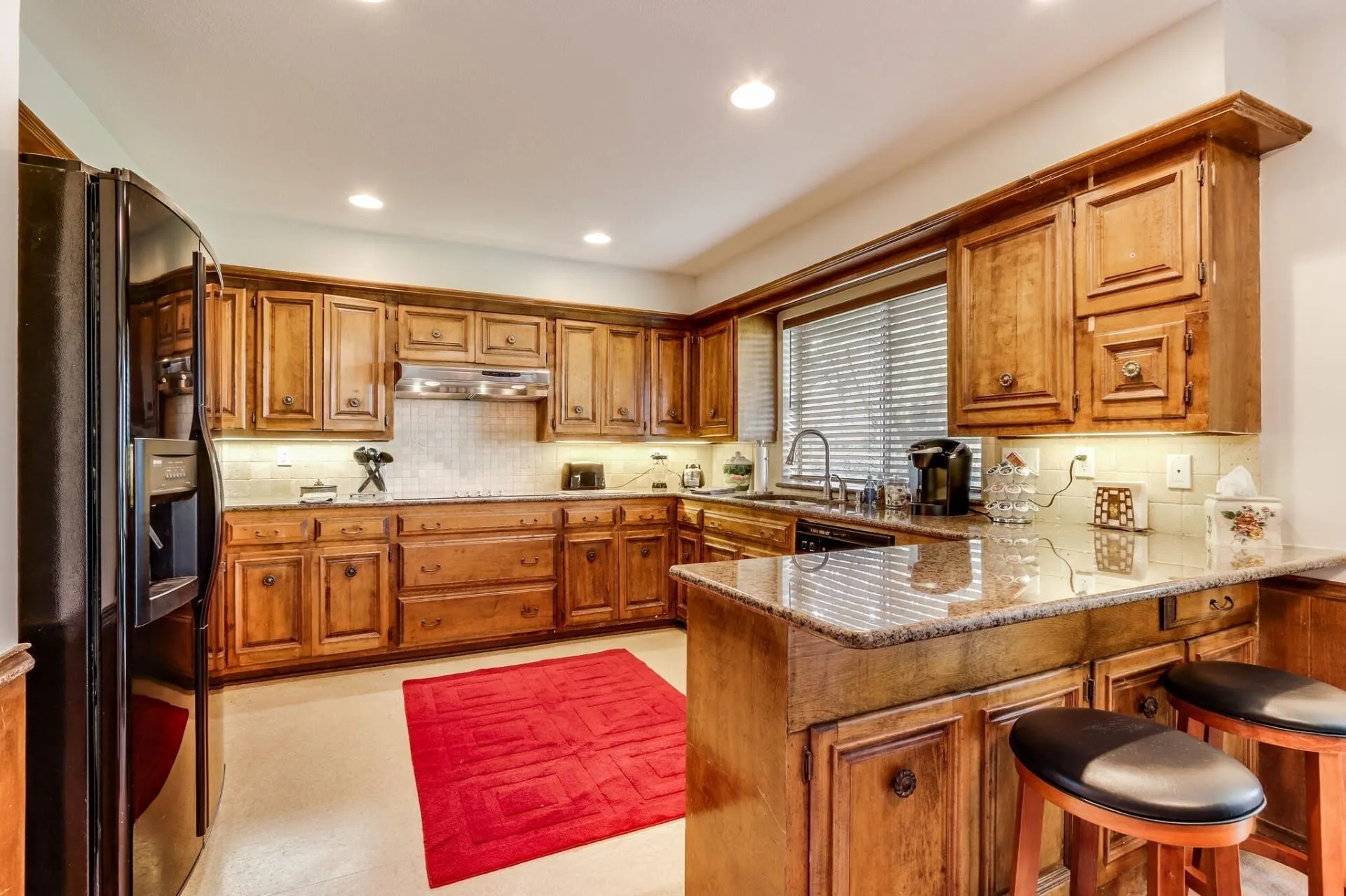 Kitchen featuring extensive wood cabinetry, granite countertops, a tiled backsplash, and recessed lighting