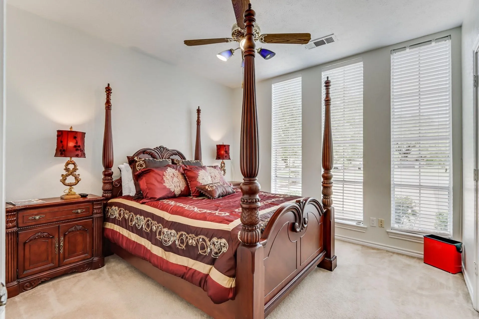 Bedroom featuring a ceiling fan with integrated lighting, three windows with blinds, light-toned wall paint, and plush carpeting