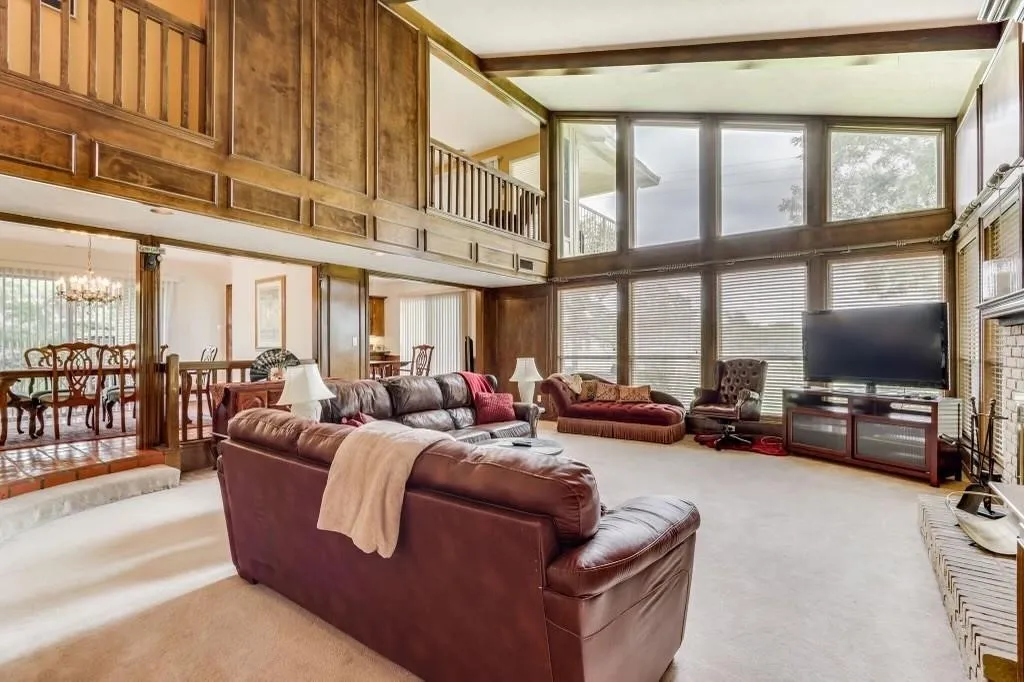 Expansive living area featuring a two-story window wall, wood paneling, and an upper-level balcony with wood railing
