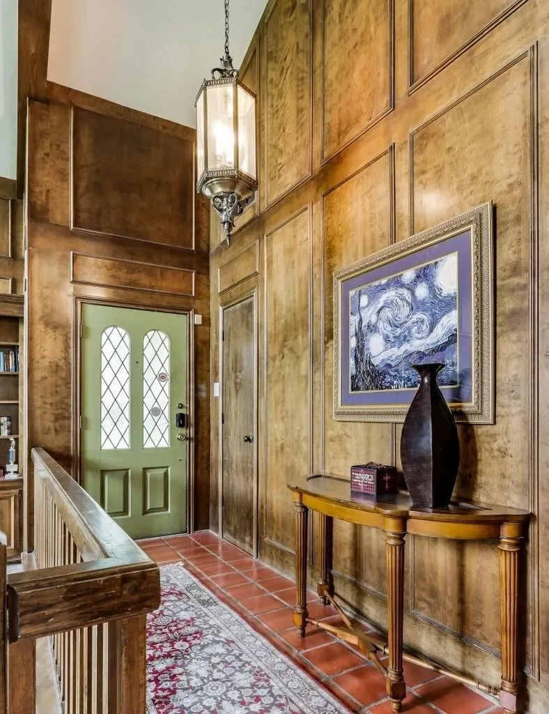 Entryway featuring extensive wood paneling, a chandelier, terracotta tile flooring, a green door with decorative lites, and wood handrailing