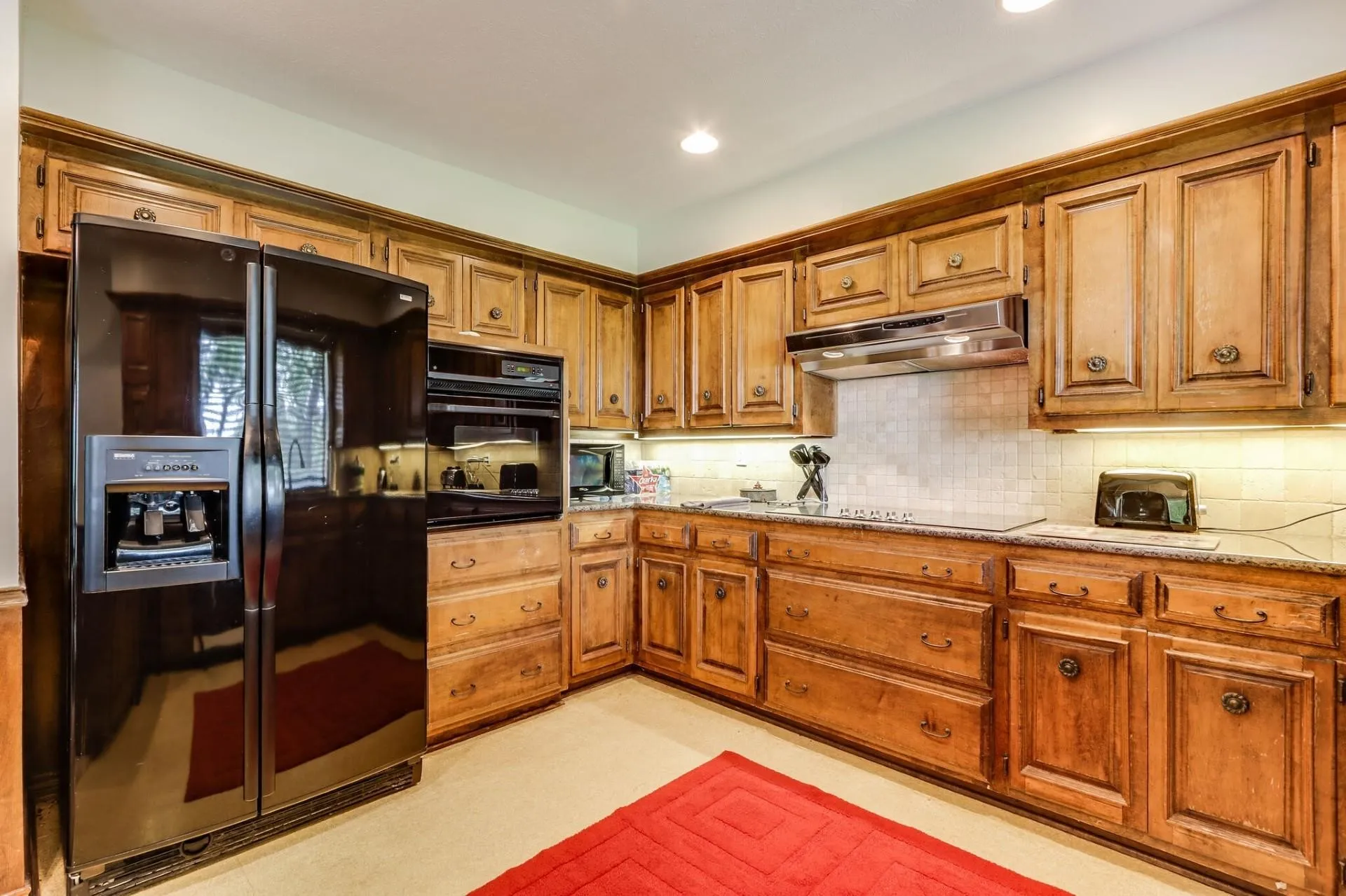 Kitchen featuring warm wood cabinetry, granite countertops, a tiled backsplash, and recessed lighting
