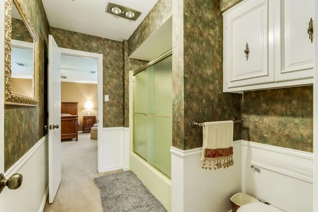 Bathroom featuring a full-size bathtub with glass enclosure, white beadboard wainscoting, and upper cabinetry with decorative hardware