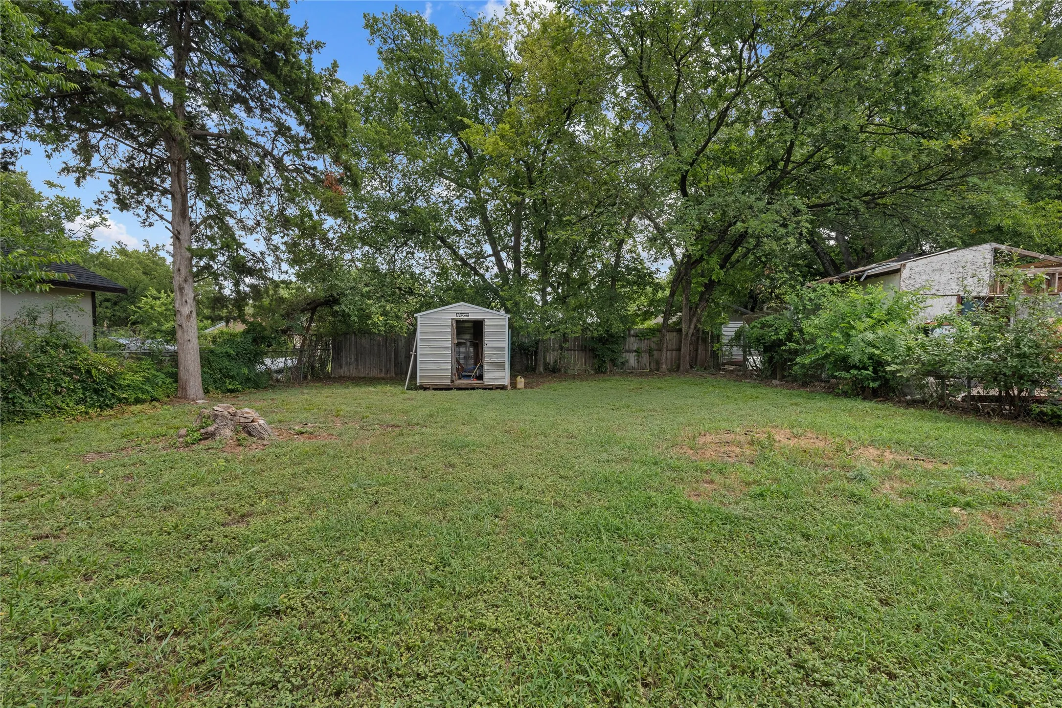 Expansive lawn area featuring a freestanding storage shed, mature trees, and a perimeter fence