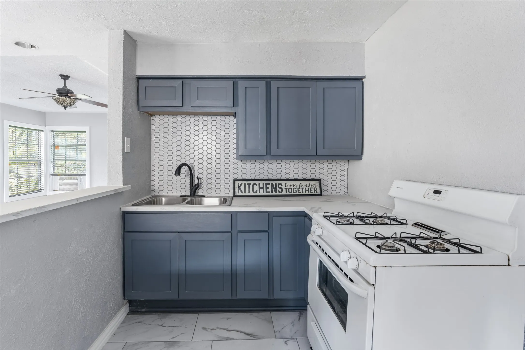 Kitchen featuring contemporary slate blue cabinetry, a white honeycomb tile backsplash, and a double basin stainless steel sink with a matte black faucet