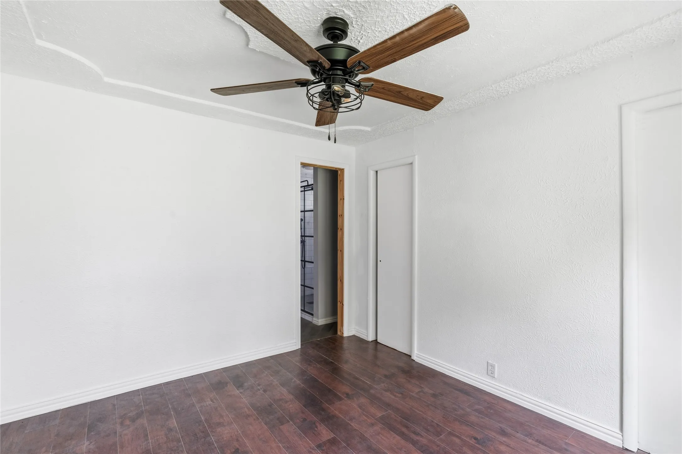 Spacious interior featuring wood-finish flooring, crisp white walls, and a ceiling fan with wood-look blades