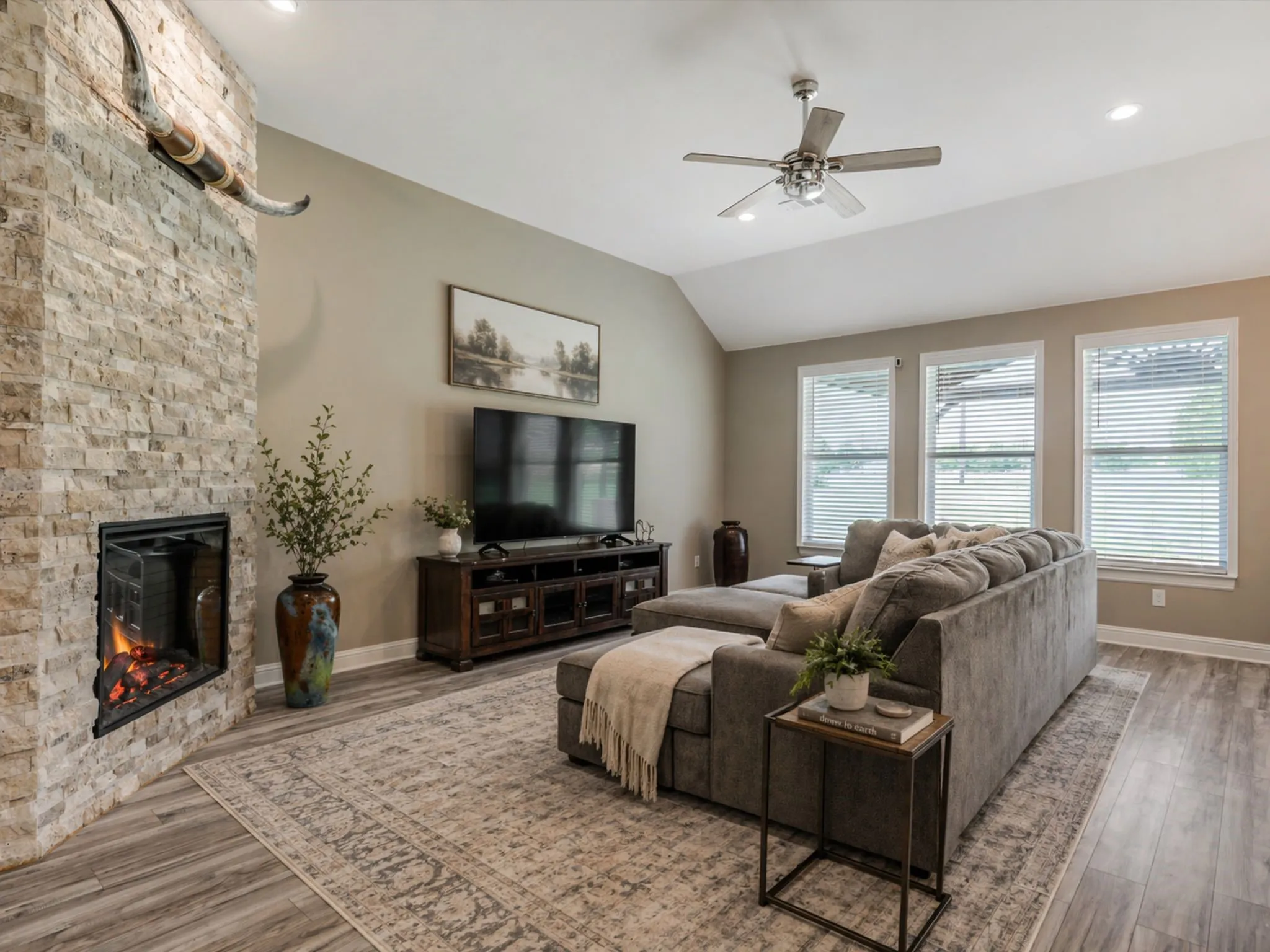 Warm and inviting living space anchored by a stunning stone fireplace and filled with natural light from a wall of windows. The open layout creates the perfect setting for both cozy nights in and effortless entertaining.