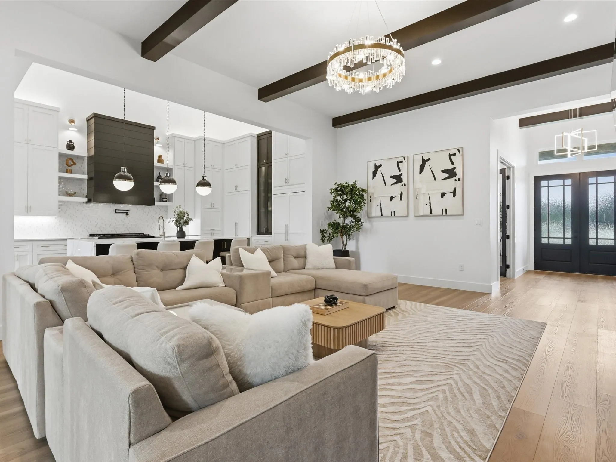 Open-concept living space featuring wood-finish flooring, exposed ceiling beams, and a contemporary chandelier