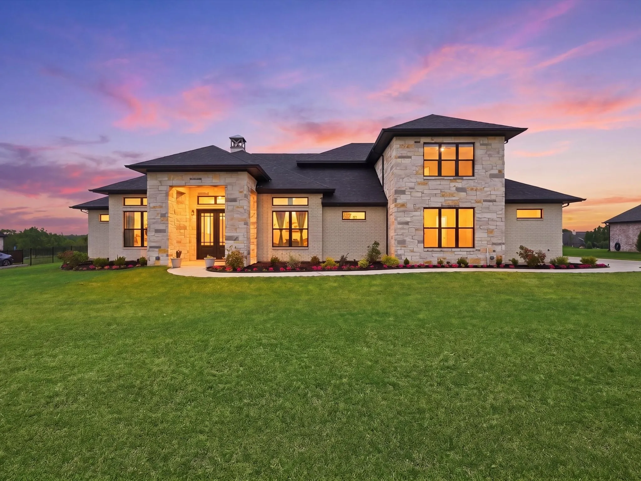 Modern architectural exterior featuring stone and stucco finishes, black-framed windows, a prominent covered entry, and a dark shingle roof