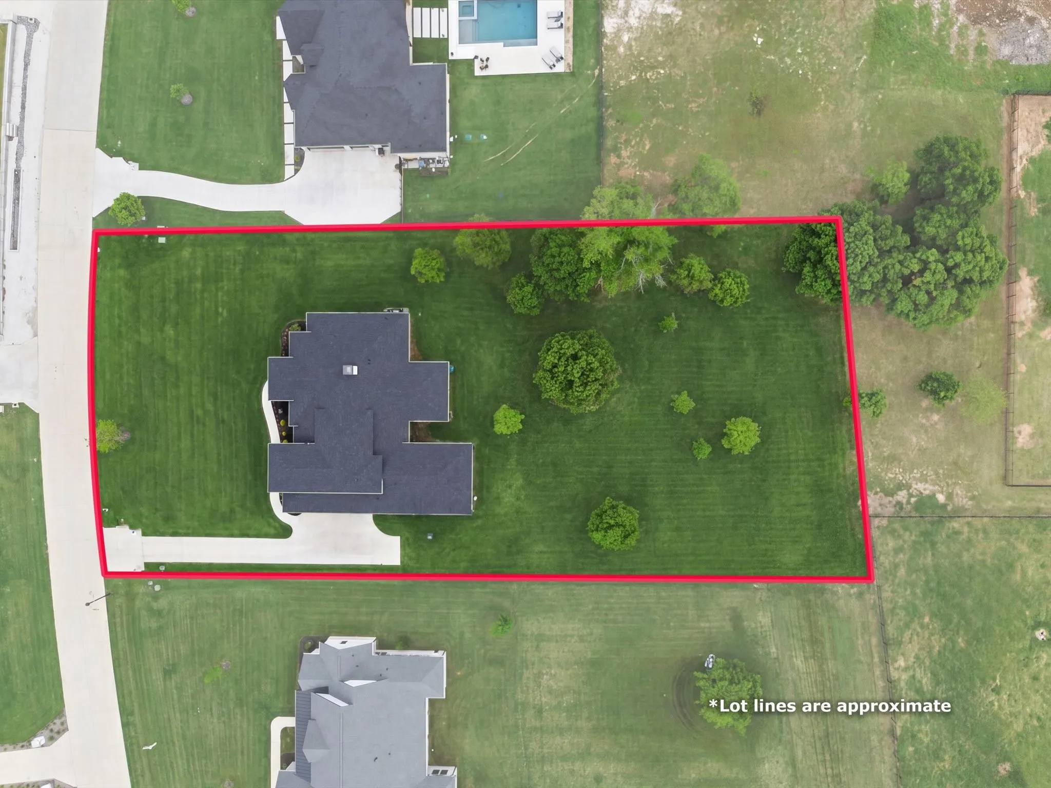 Expansive lot with a modern residence featuring a dark shingle roof and a concrete driveway