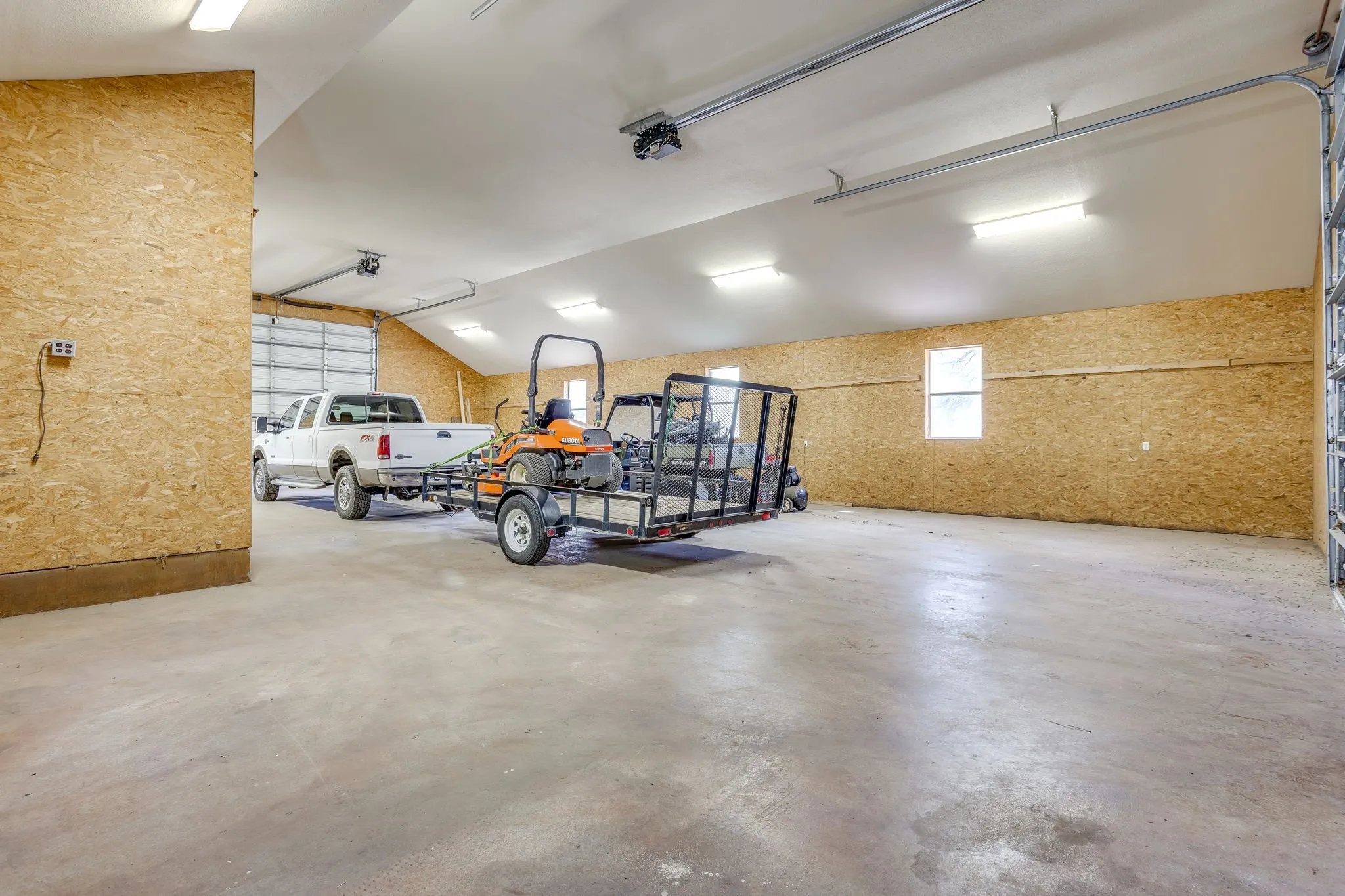 Spacious garage with exposed wood-finish walls, concrete flooring, multiple windows, and overhead lighting