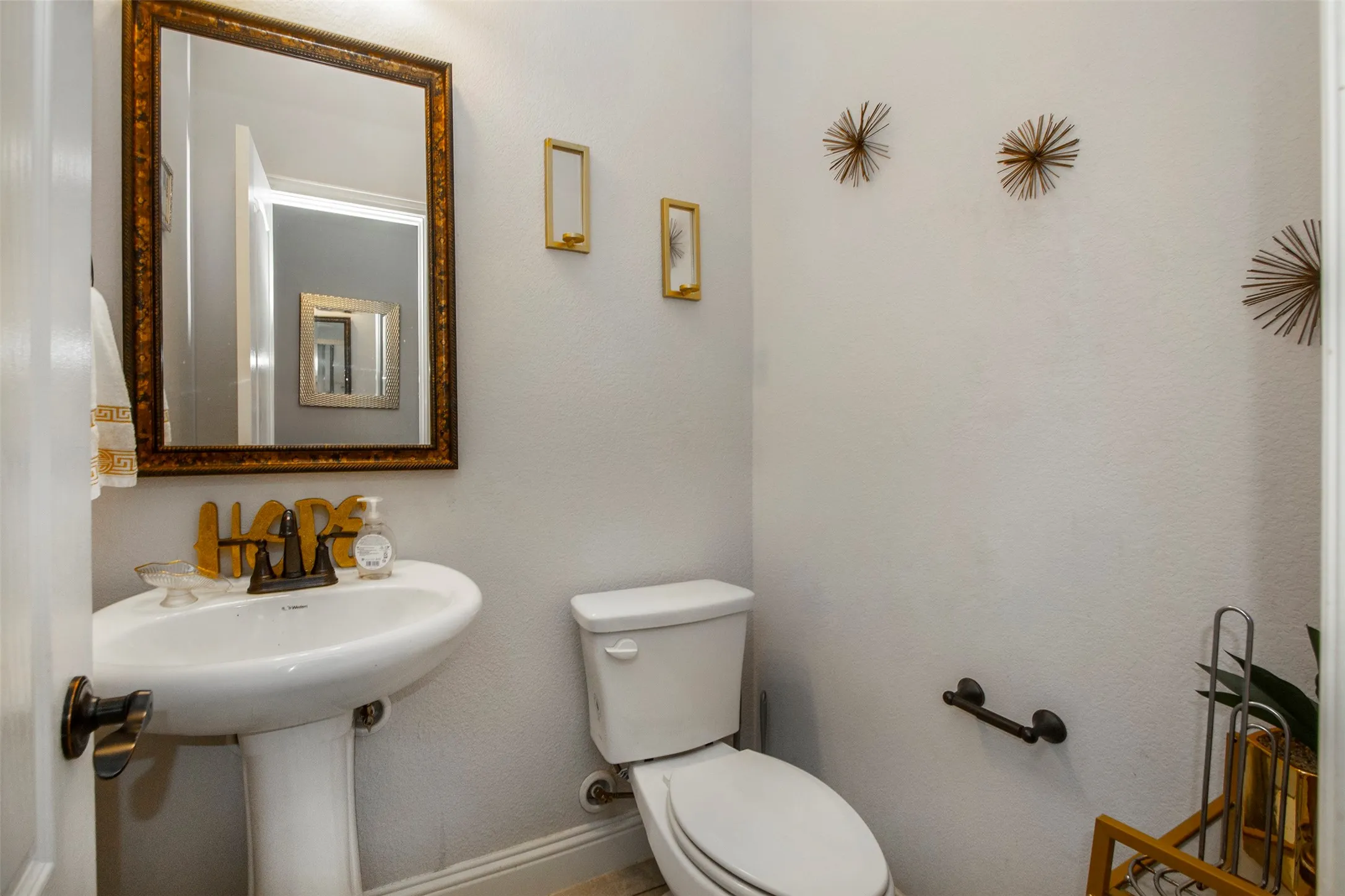 Pedestal sink with dark bronze faucet, framed mirror, and white toilet