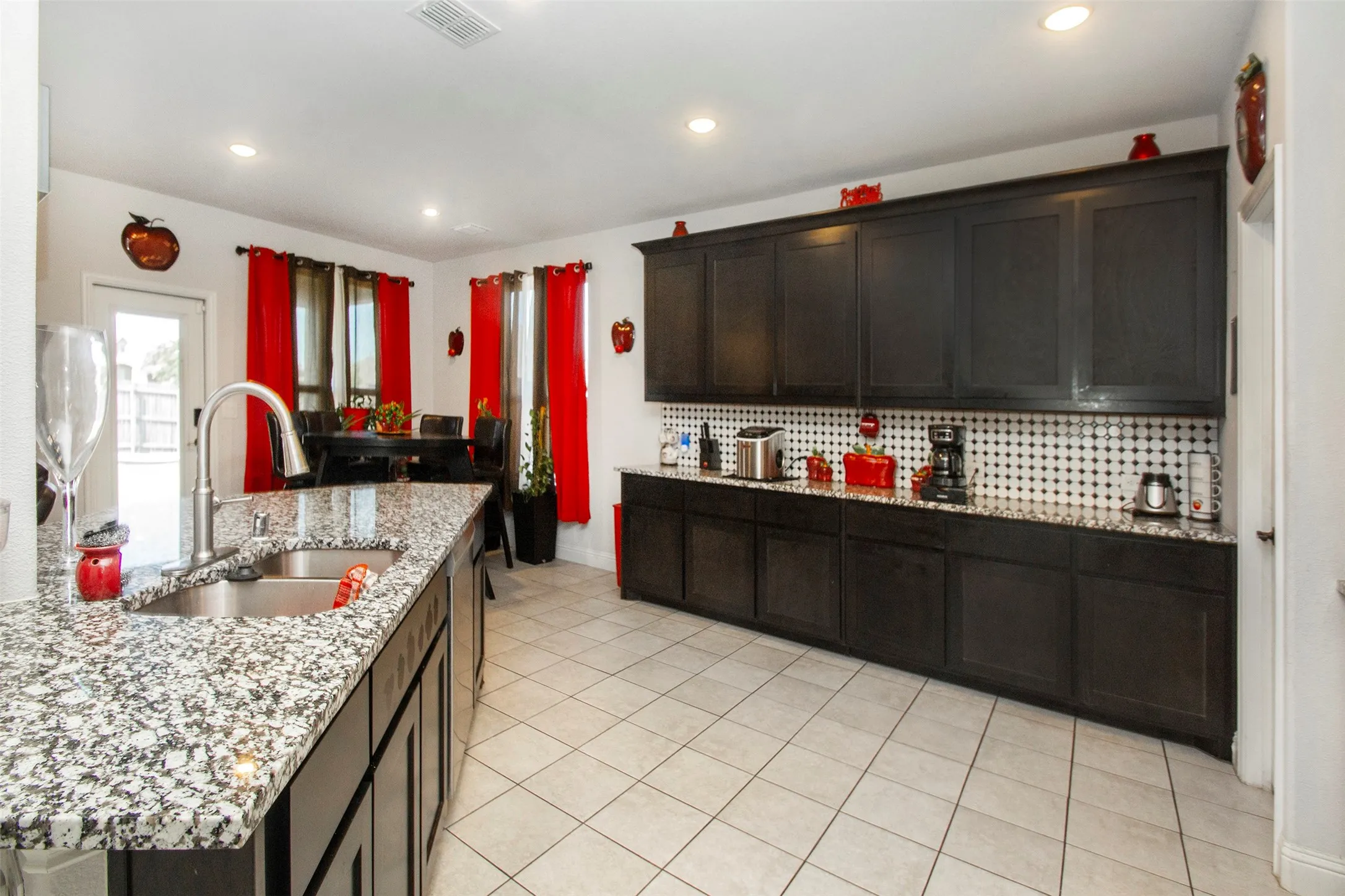 Kitchen featuring granite countertops, a double basin stainless steel sink with a gooseneck faucet, dark wood cabinetry, a tiled backsplash, and recessed lighting