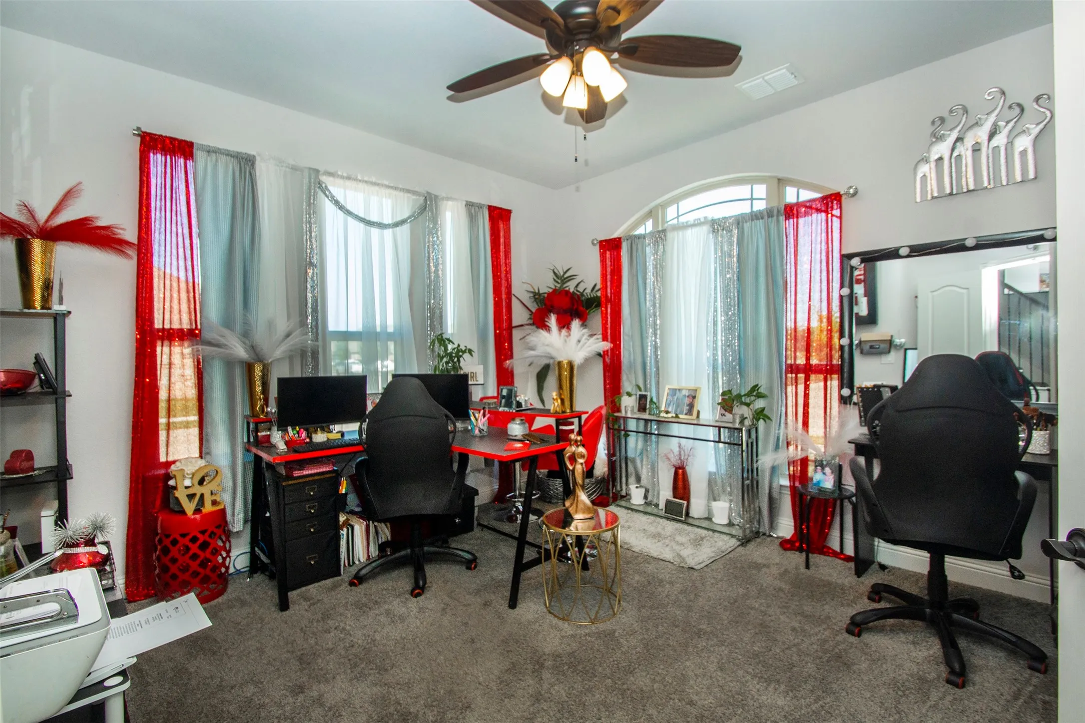 Carpeted room featuring a ceiling fan, arched transom window, and a built-in vanity with mirror and lighting