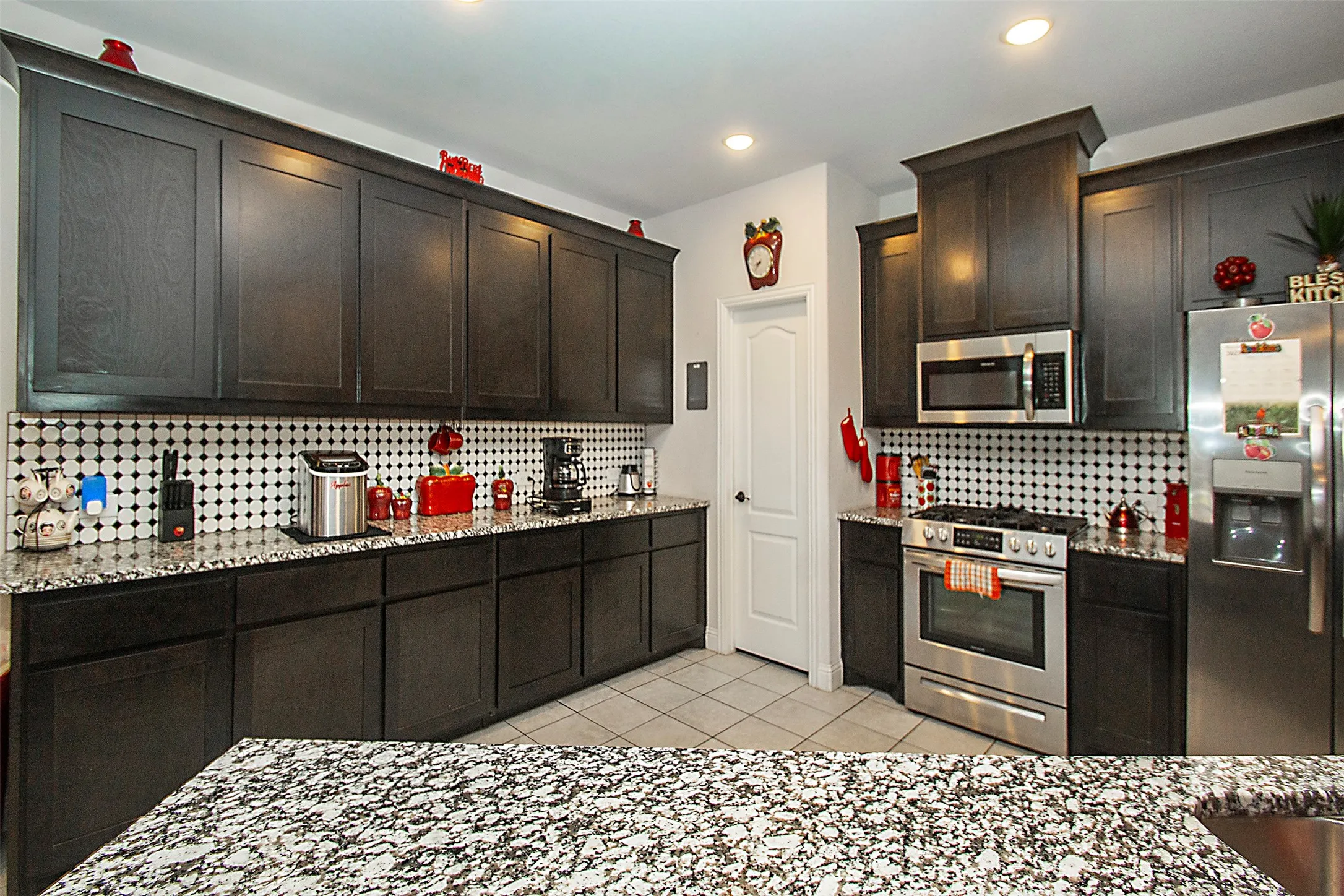 Kitchen featuring dark wood-finish cabinetry, speckled stone countertops, and a white and black mosaic tile backsplash