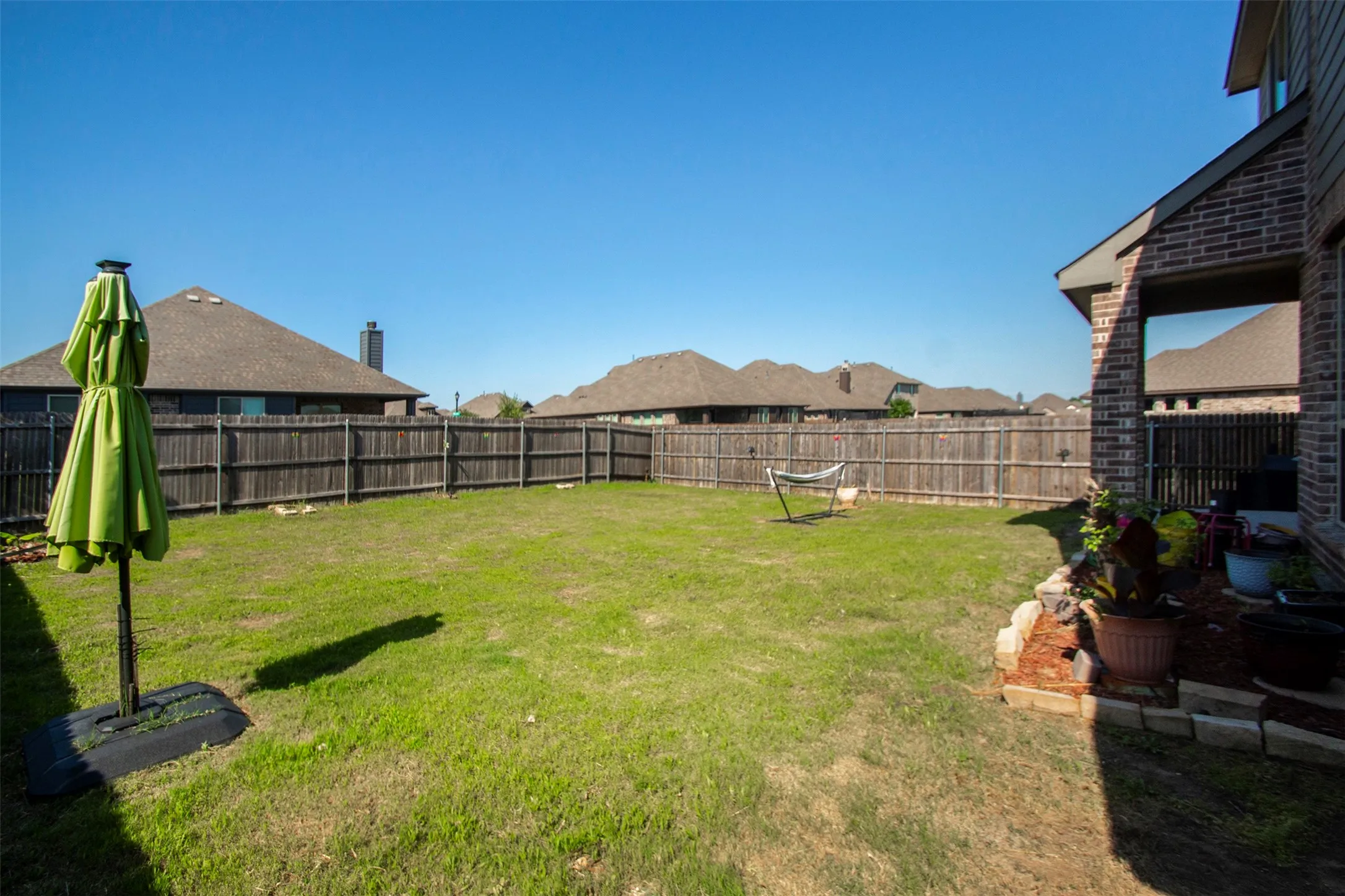 Expansive fenced backyard featuring a grassy lawn, wood privacy fencing, and a brick exterior with a covered patio area