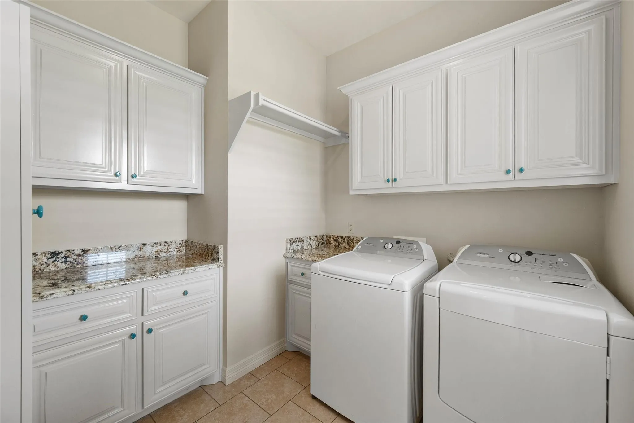 Laundry area featuring white cabinetry, granite-finish countertops, tile flooring, and integrated shelving