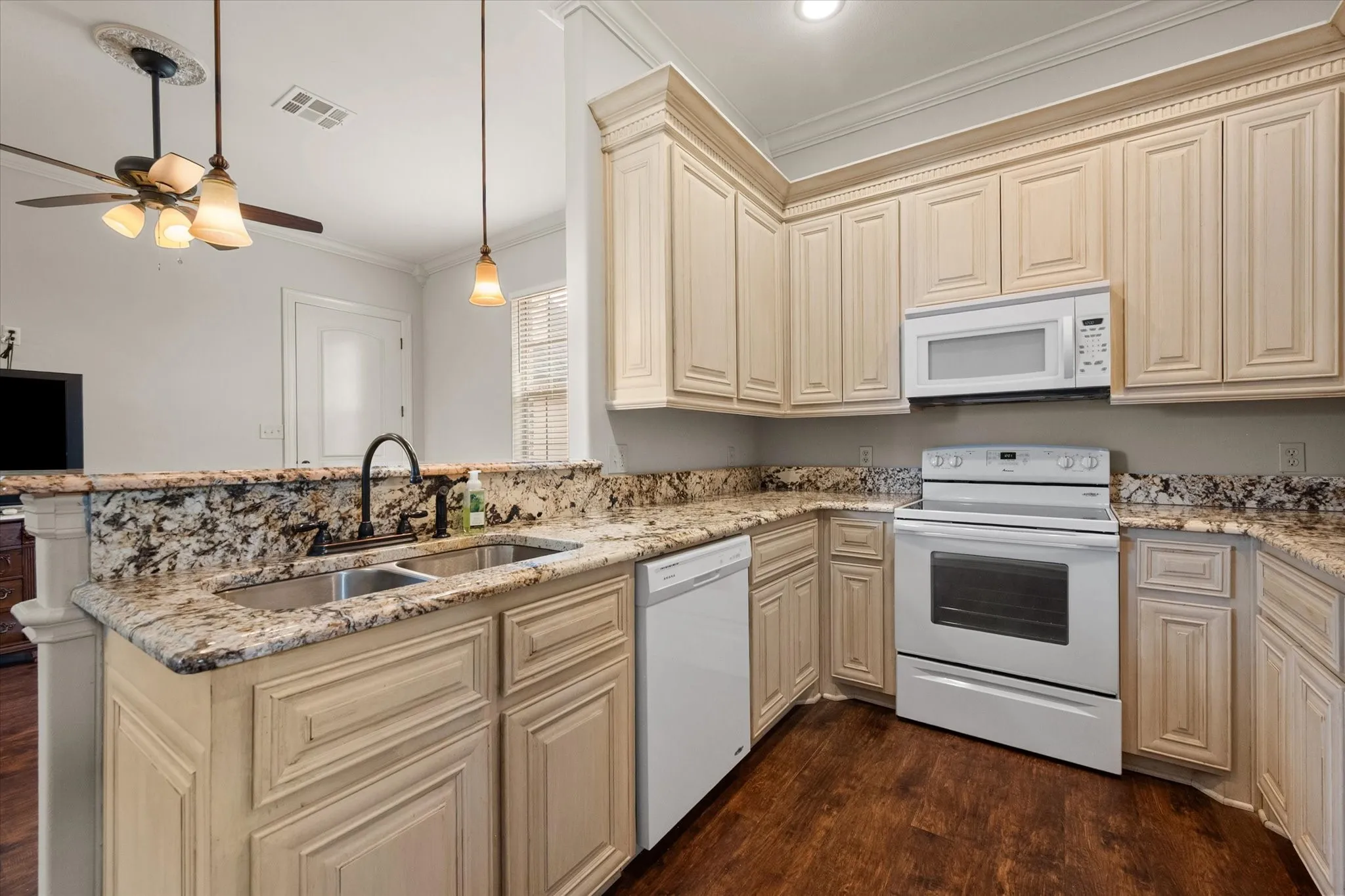 Kitchen featuring extensive cabinetry, granite countertops, a double basin sink with a gooseneck faucet, white appliances including an oven range and microwave, and wood-finish flooring