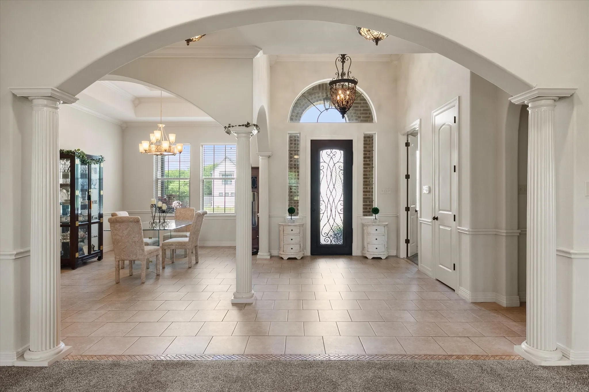 Spacious foyer featuring arched doorways, classic fluted columns, and light tile flooring
