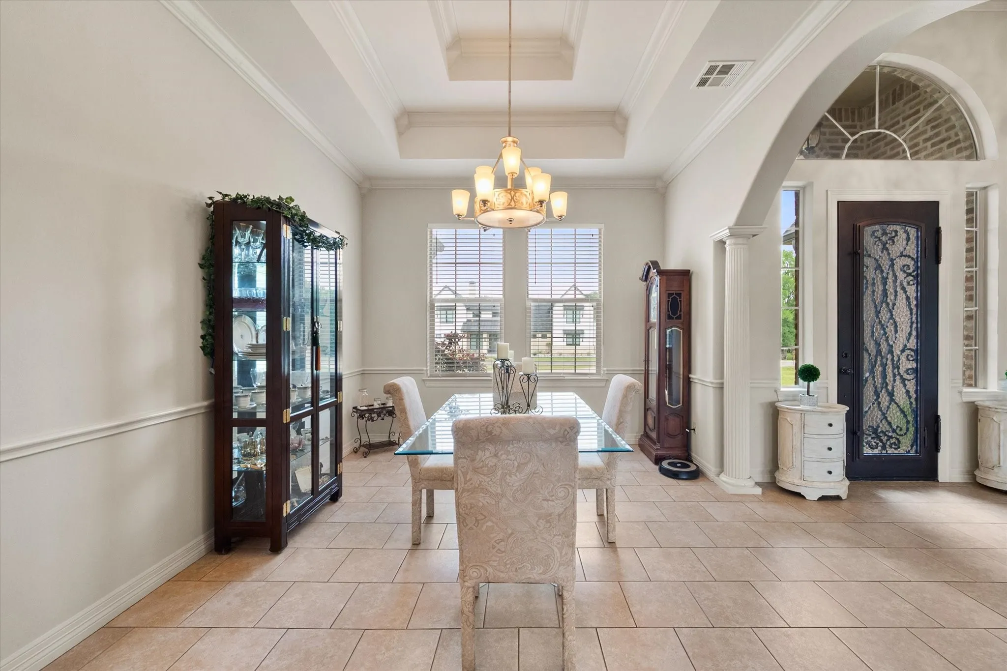 Spacious dining area featuring a tray ceiling with a chandelier, tile flooring, crown molding, and wainscoting