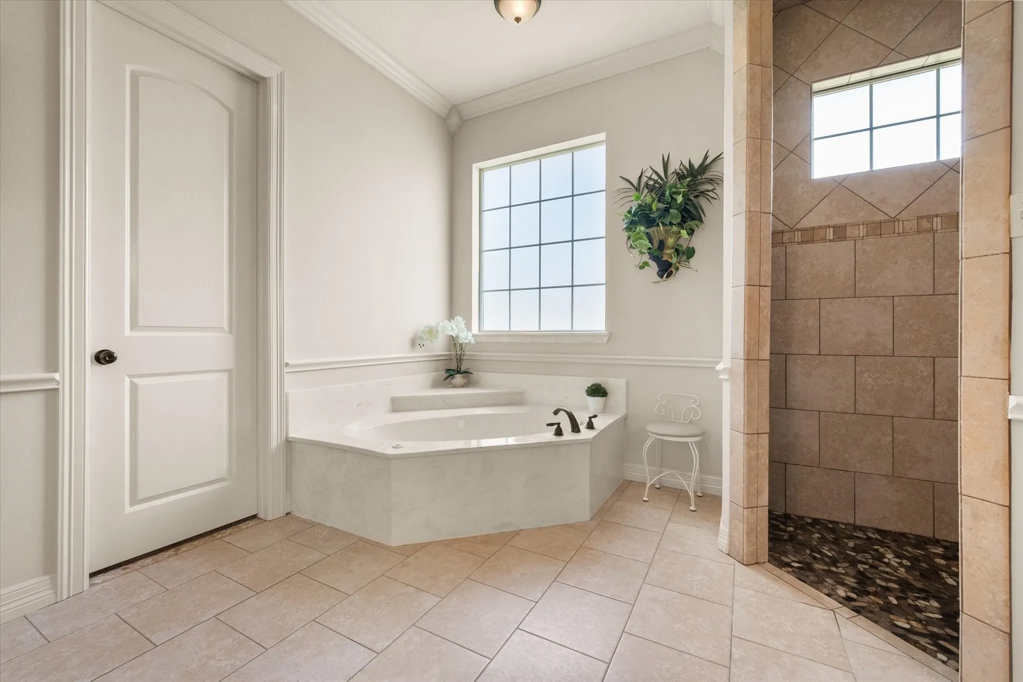 Bathroom featuring a corner soaking tub with a stone surround, a separate walk-in shower with stone tile walls and a pebble floor, and tile flooring
