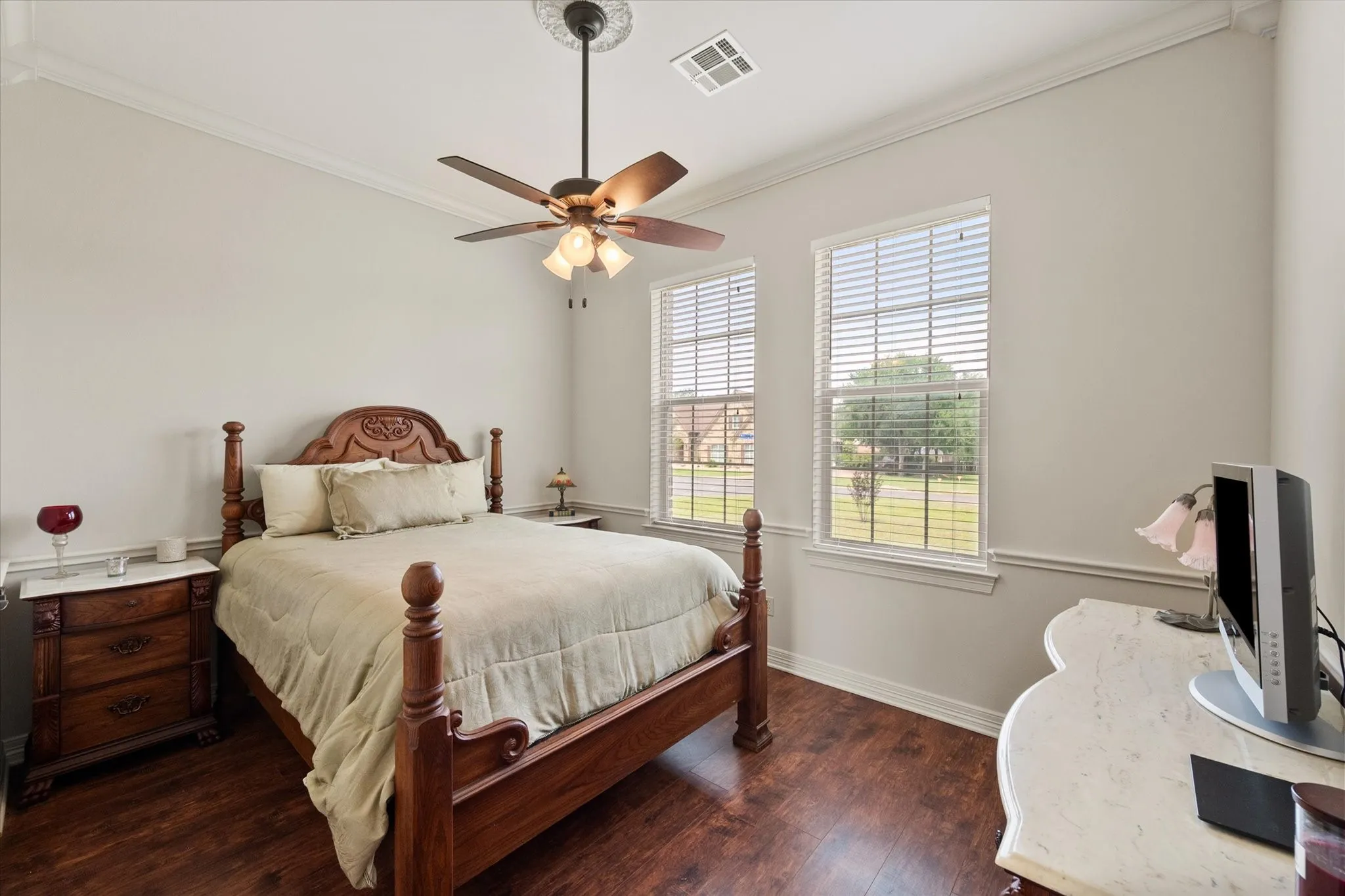 Bedroom in the guest apartment featuring wood-finish flooring, two windows with blinds, and crown molding