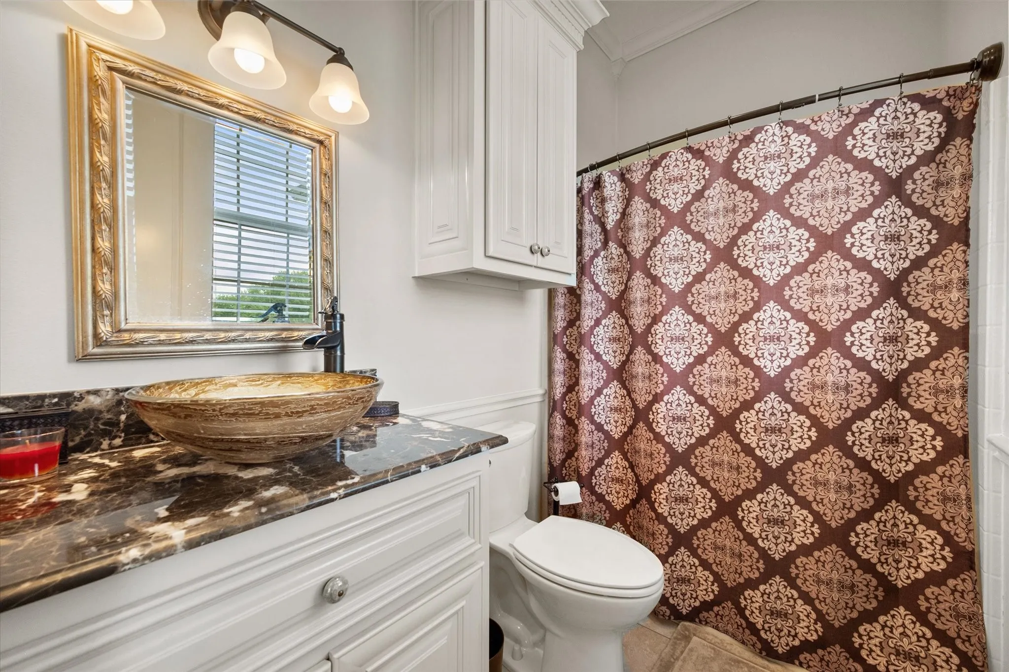 Ensuite bathroom featuring a vessel sink, dark patterned countertop, white cabinetry, decorative mirror, and a walk-in shower.