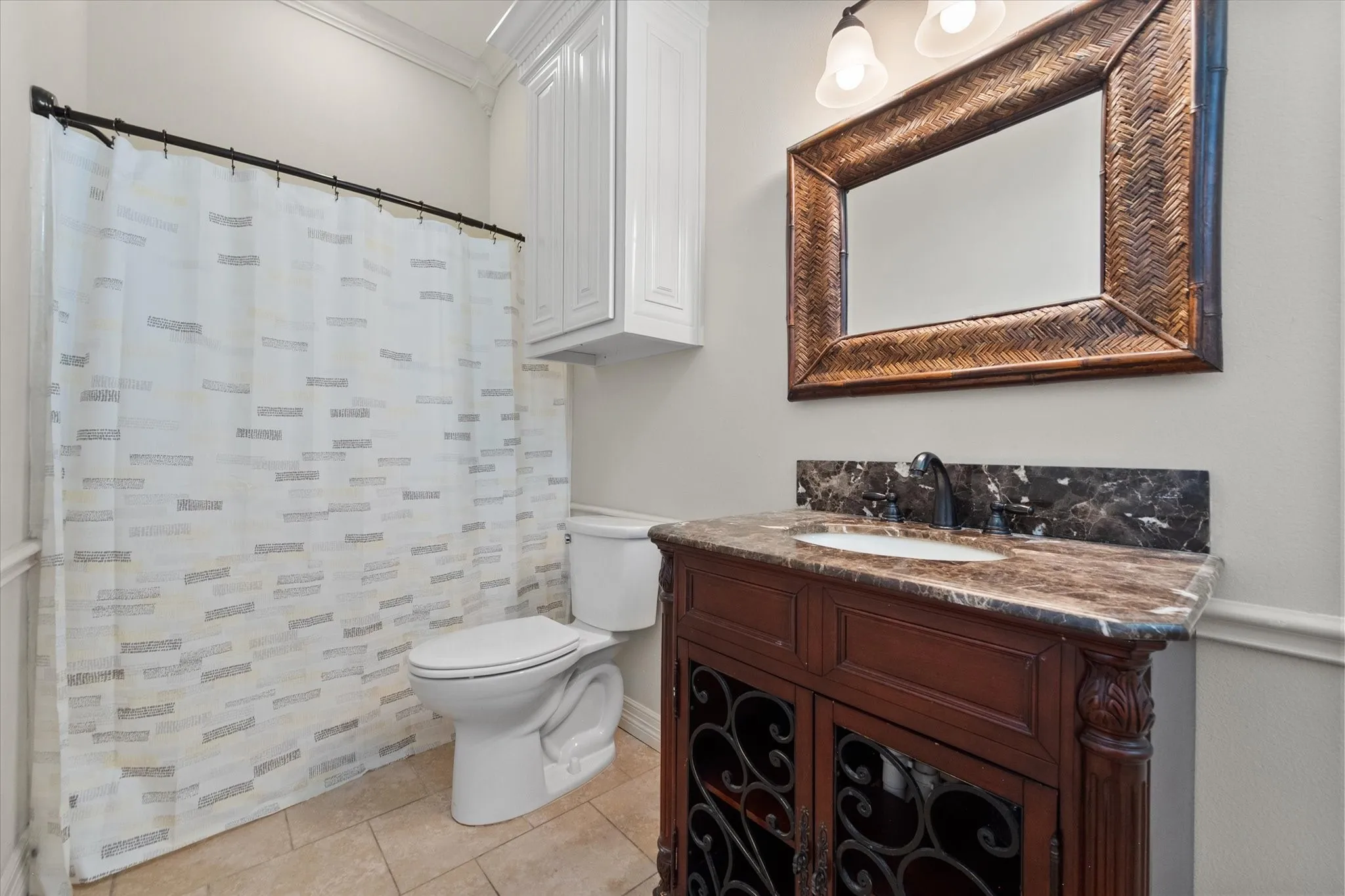 Bathroom featuring a decorative wood-finish vanity with an integrated sink, a dark veined countertop with matching backsplash, and a framed mirror. Also has a full laundry closet with a washer and dryer