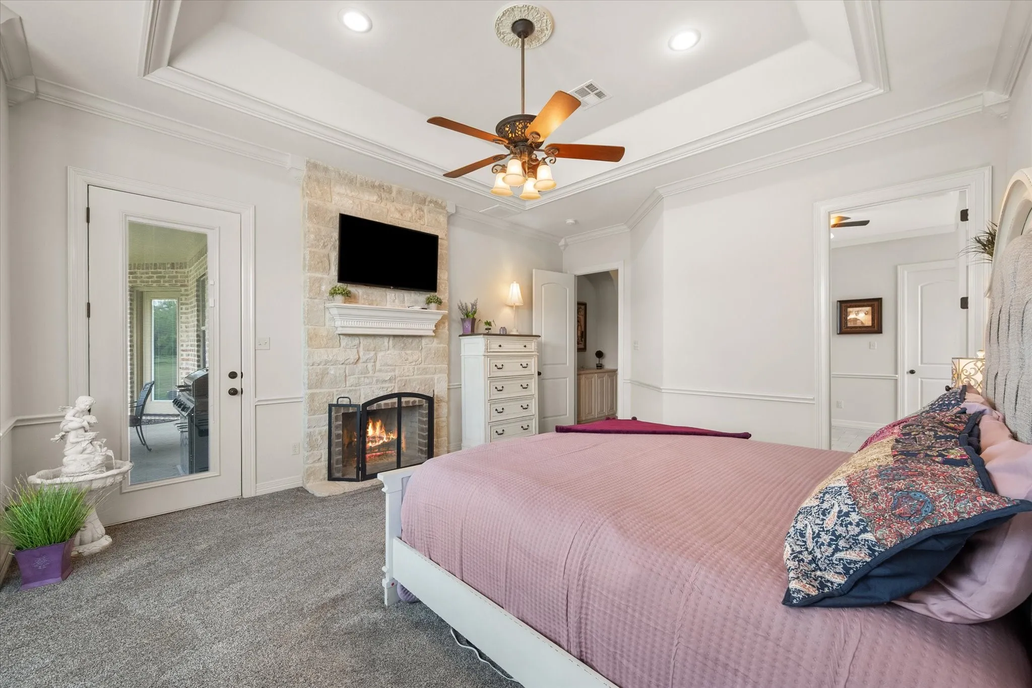 Spacious primary bedroom with a tray ceiling, stone fireplace, and recessed lighting
