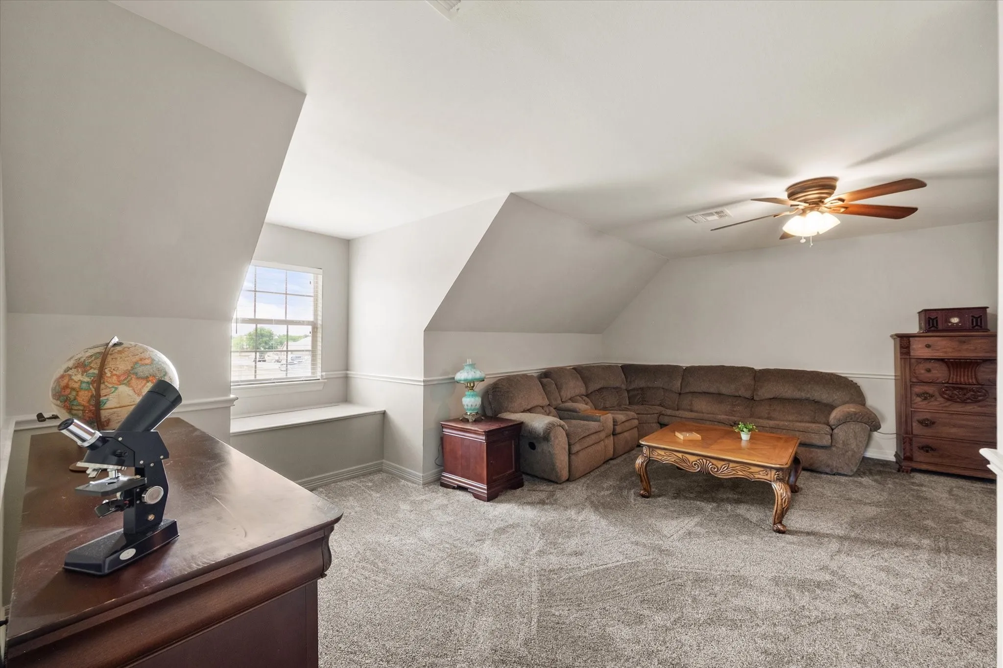Upstairs room can be used a bedroom, playroom, etc. Features a ceiling fan, a window with an integrated window seat, and sloped ceilings