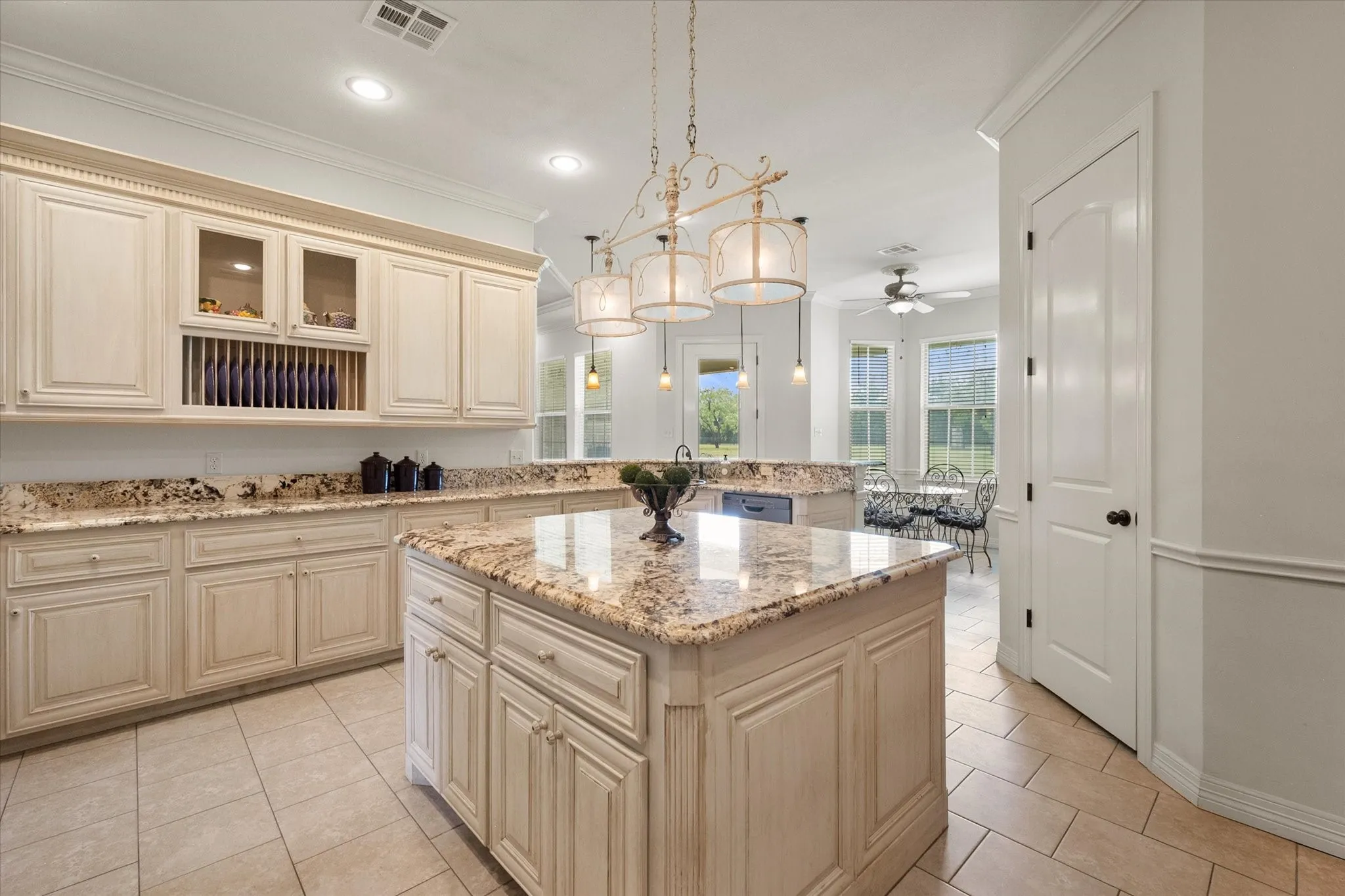 Spacious kitchen featuring a central island with granite countertops, extensive cabinetry, tile flooring, built-in plate rack, and recessed lighting