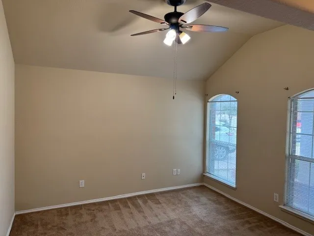 Vaulted ceiling room featuring two arched windows with blinds, plush brown carpet, and a ceiling fan with integrated lighting